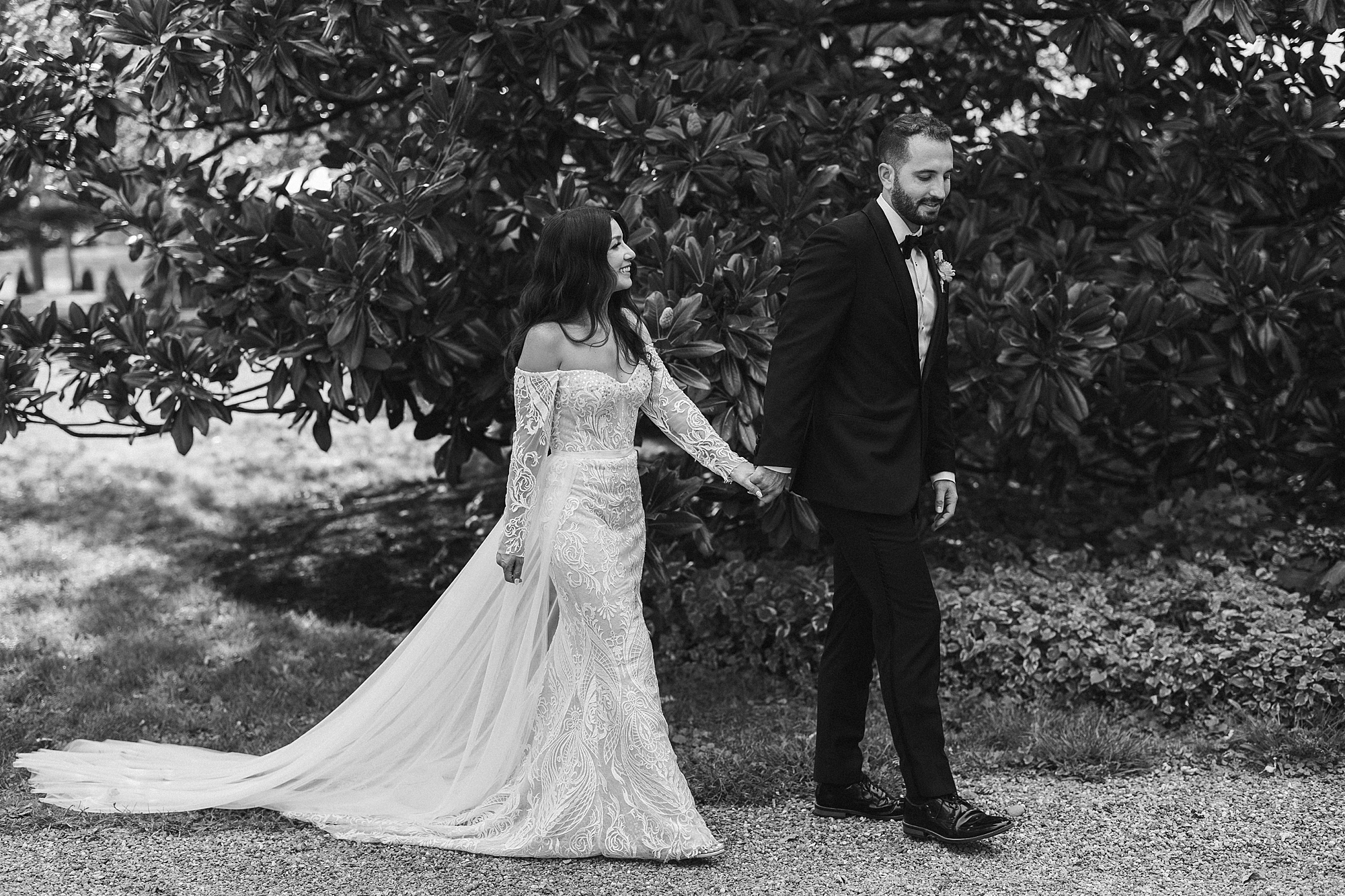 groom walks with bride's hand in his through gardens at The Cypress House