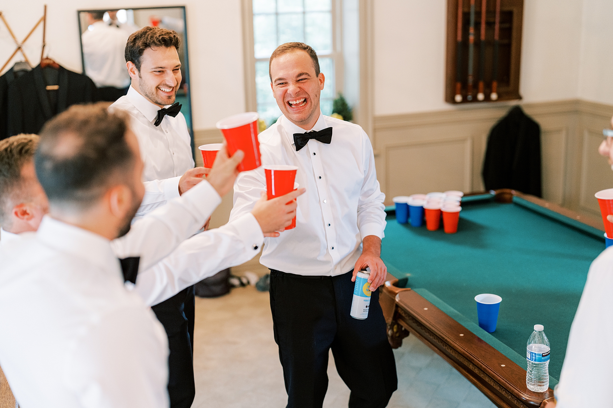 groomsmen laugh together with red solo cups by pool table 