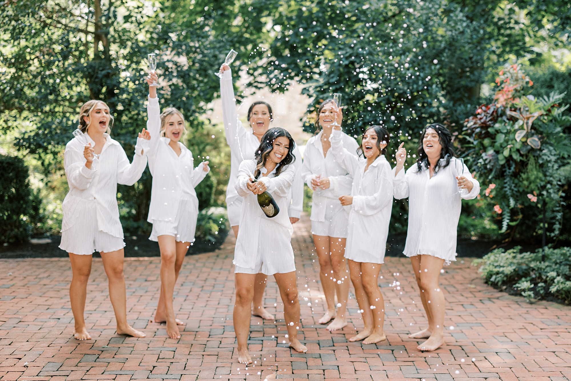 bride pops champagne while bridesmaids in white pajamas cheer 