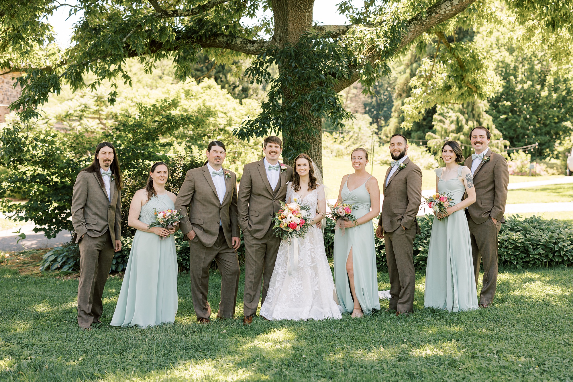 bride and groom stand with wedding party in tan and mint attire