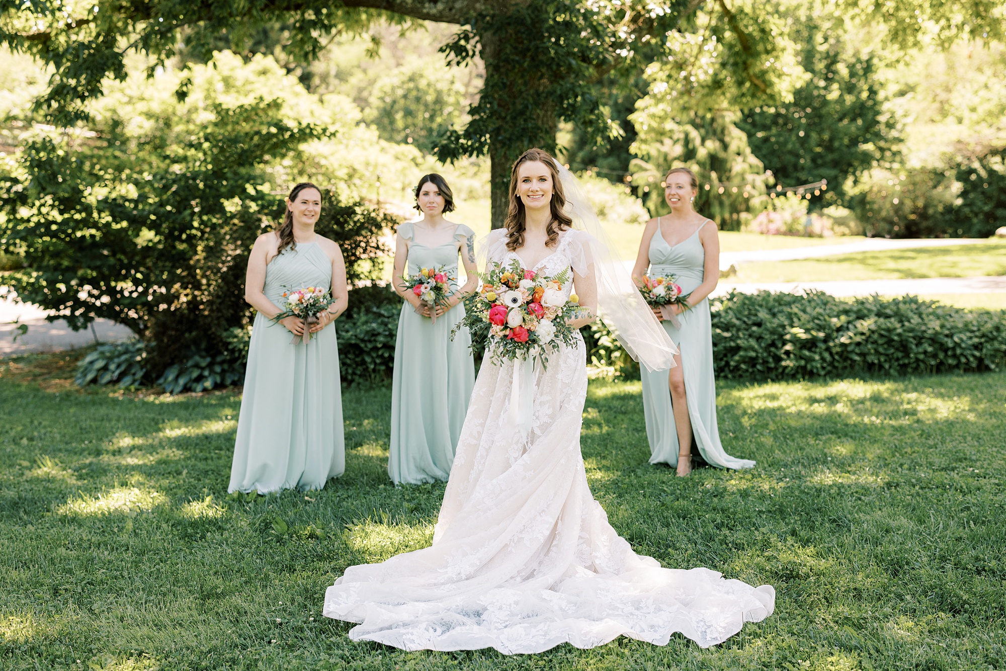 bride stands in wedding gown with lace cap sleeves in front of bridesmaids in mint gowns
