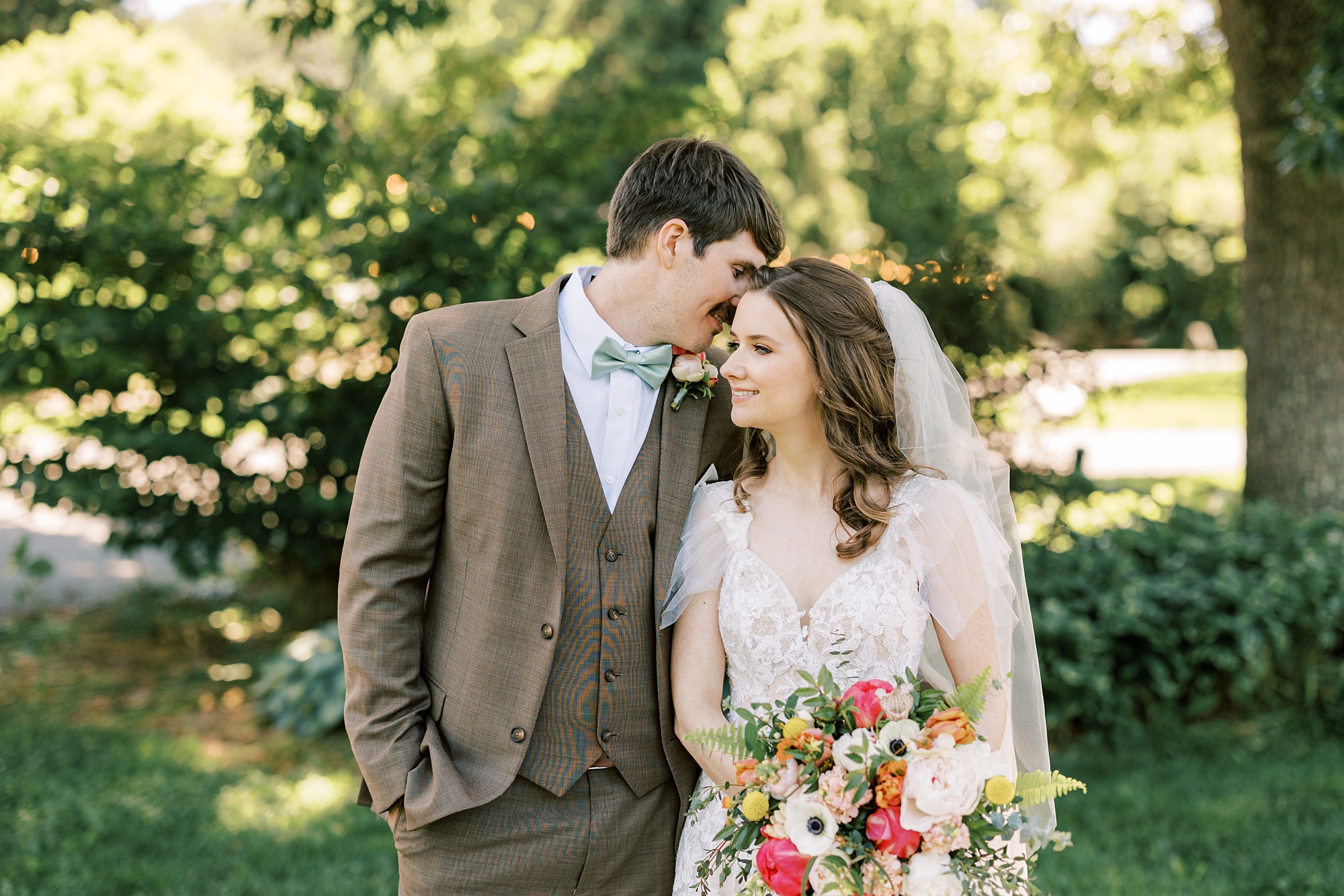 groom in brown suit whispers in bride's ear at Tyler Arboretum