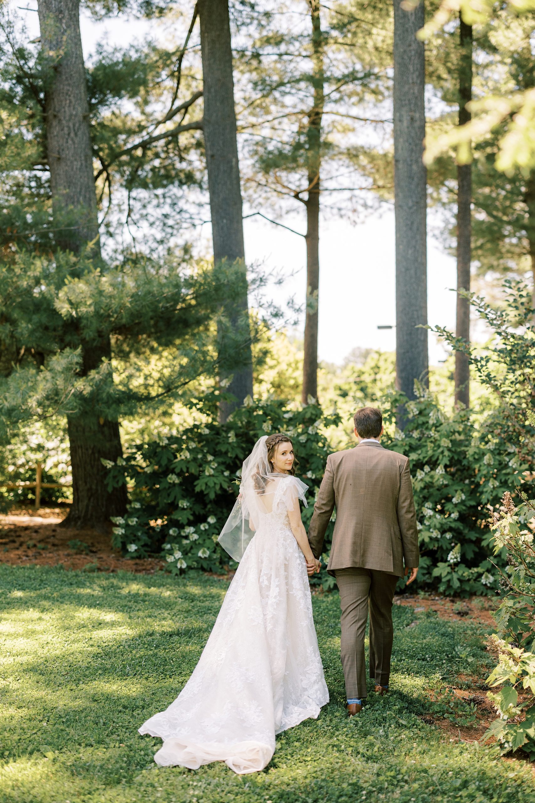 couple holds hands walking towards woods at Tyler Arboretum