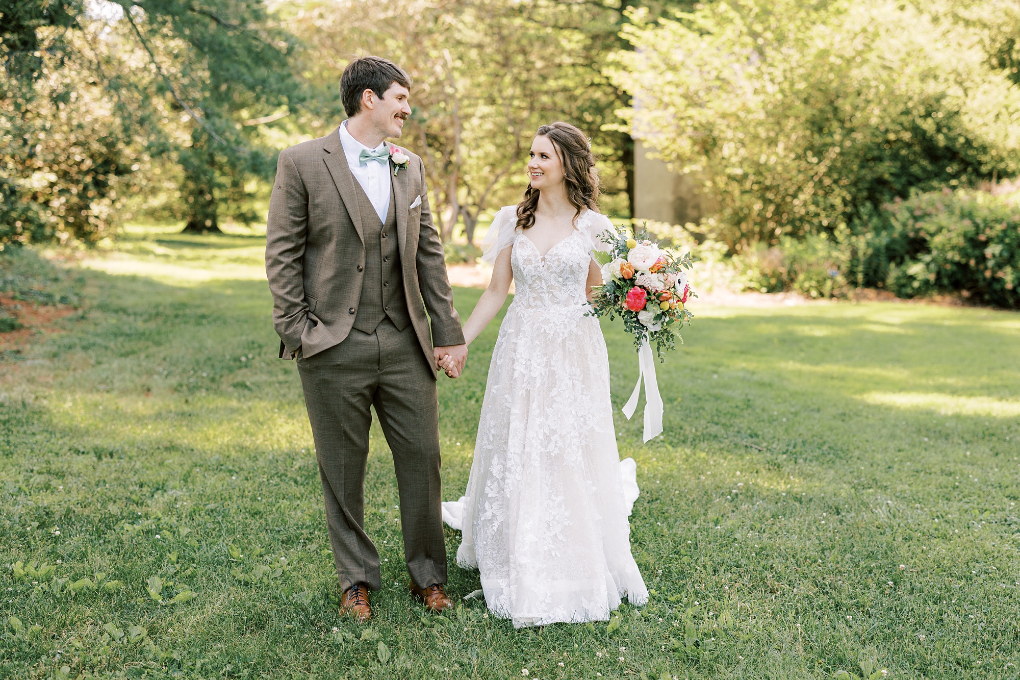 newlyweds hold hands walking on lawn at Tyler Arboretum
