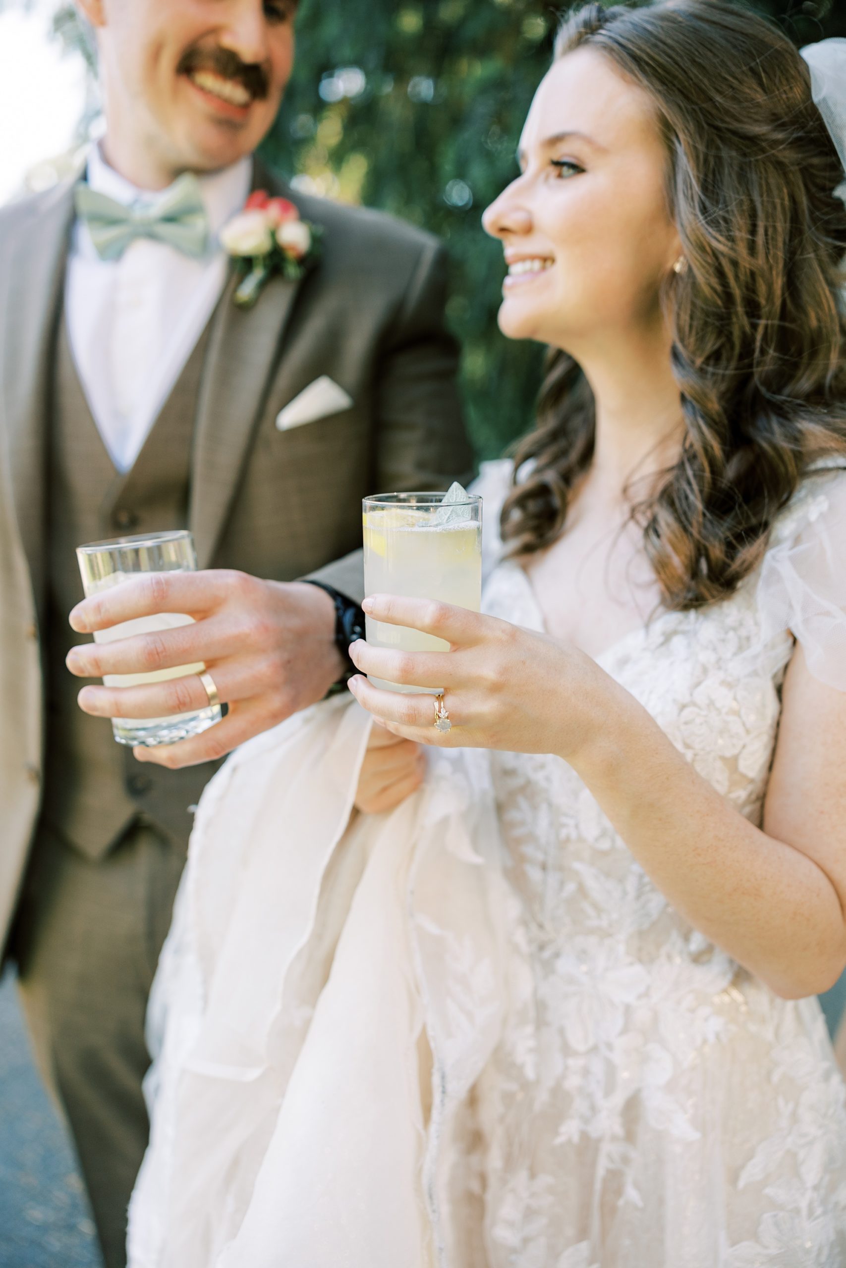 newlyweds hold glasses of lemonade showing off wedding rings 