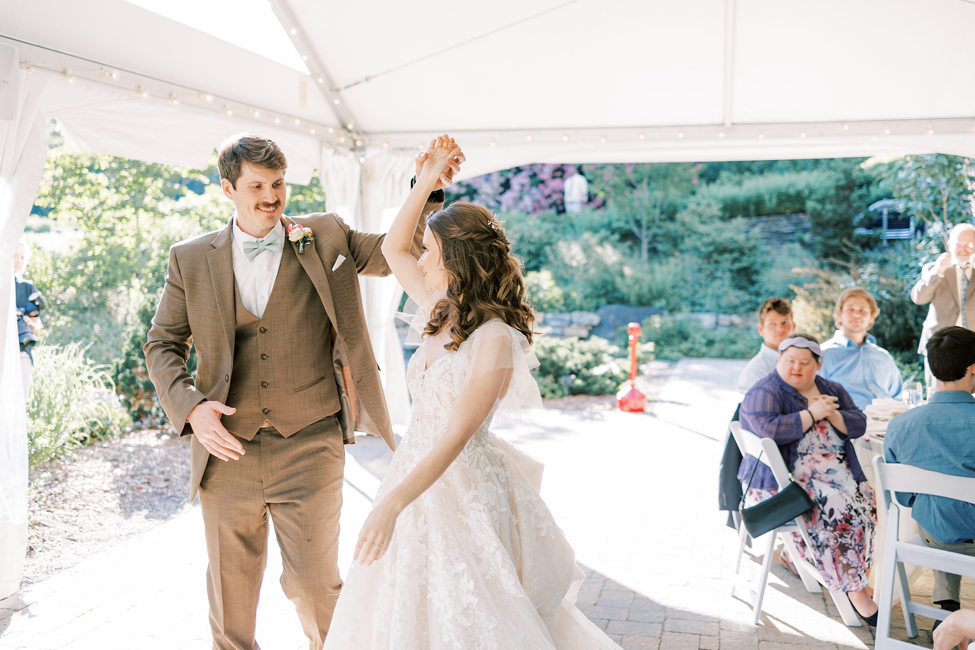 groom twirls bride walking into tented wedding reception at Tyler Arboretum