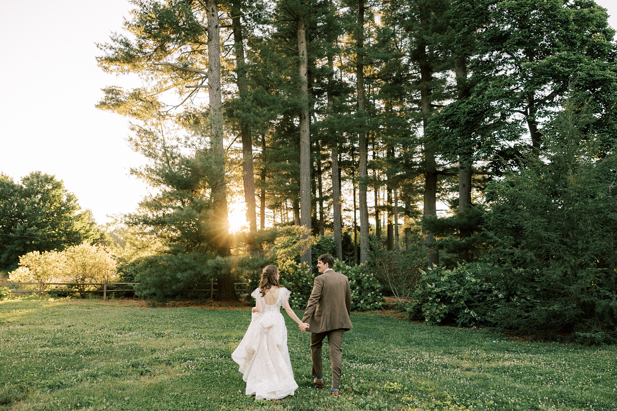 bride and groom walk towards trees at sunset 