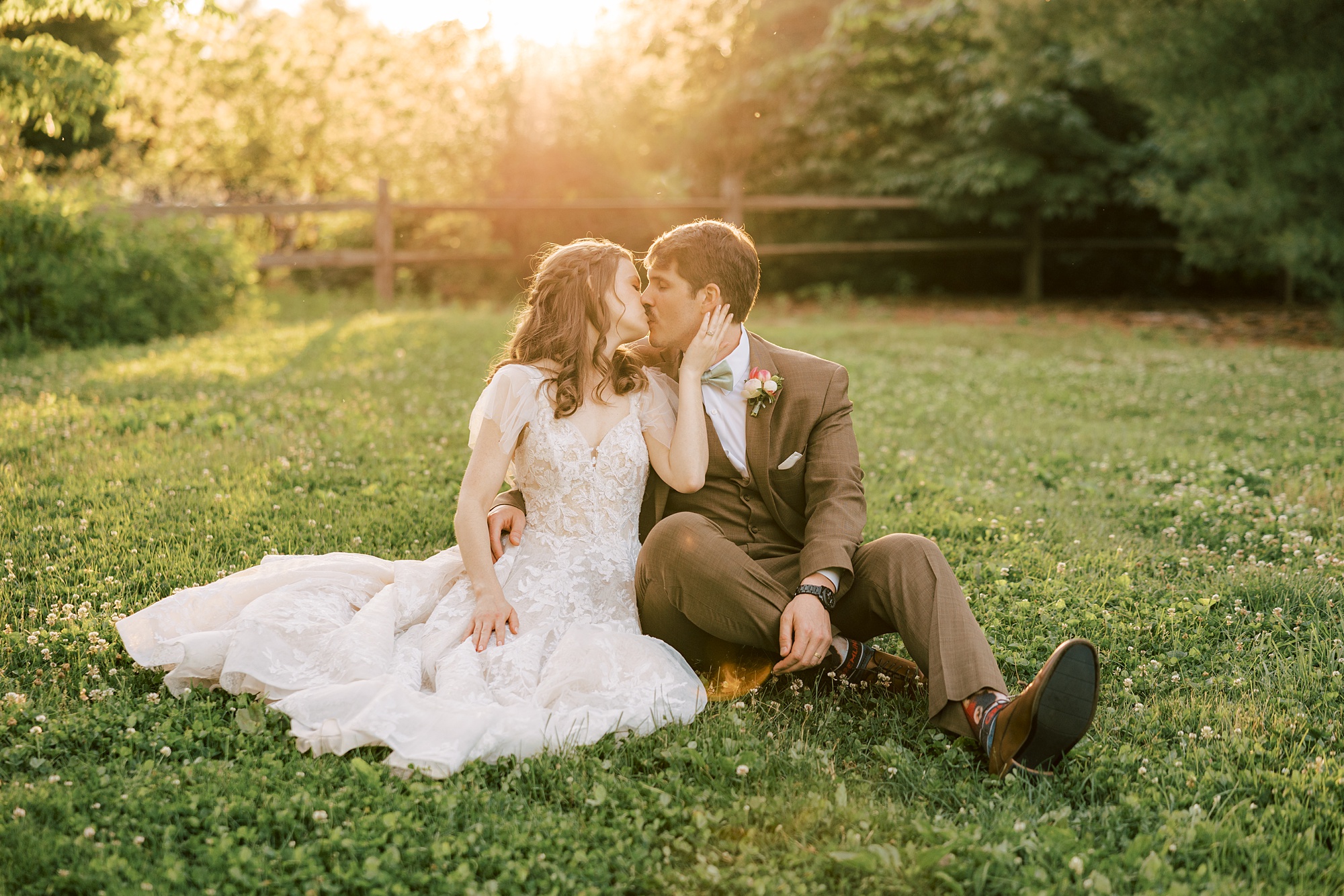 newlyweds sit on lawn at sunset kissing at Tyler Arboretum 