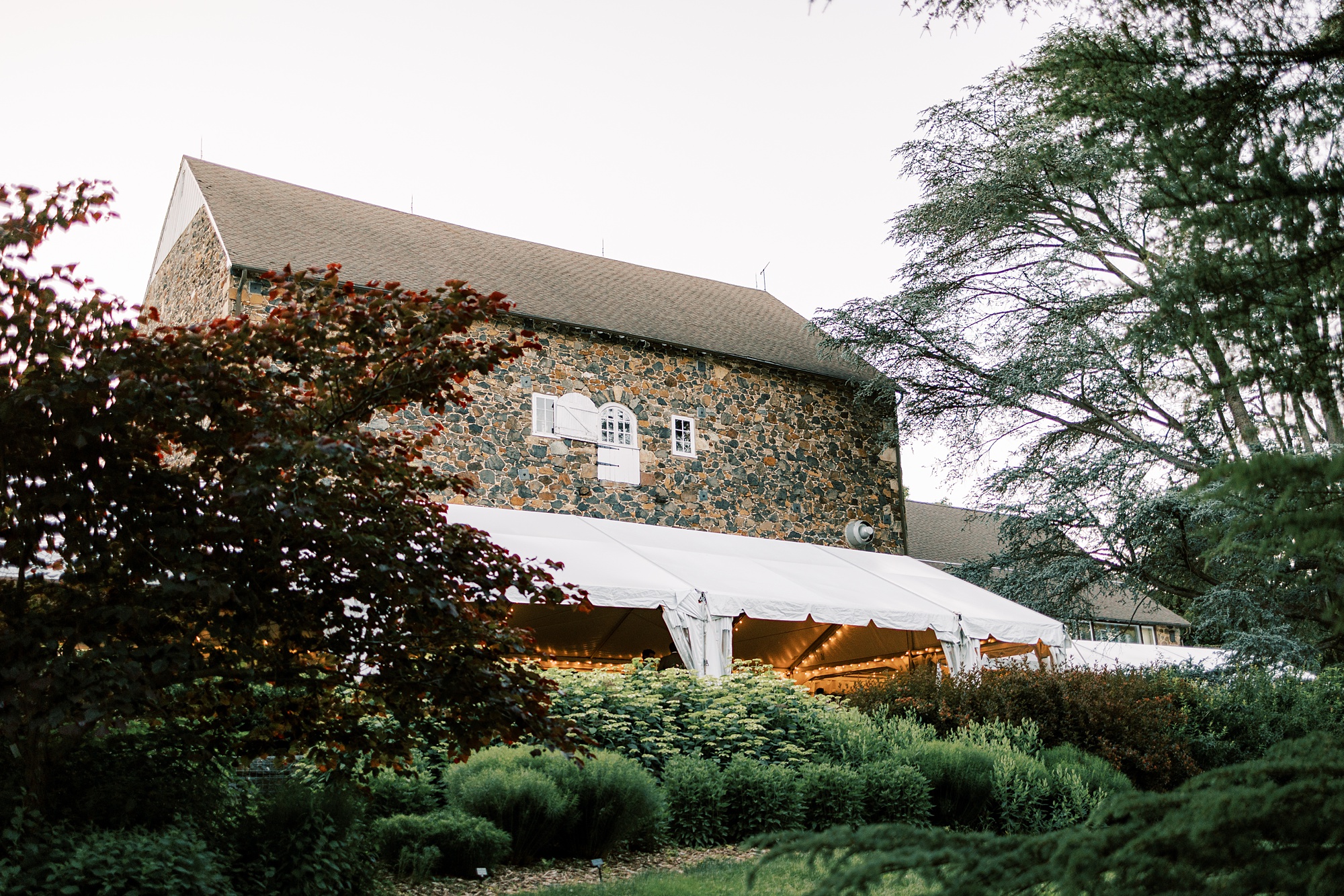 wedding reception under white tent along side of stone barn at Tyler Arboretum 