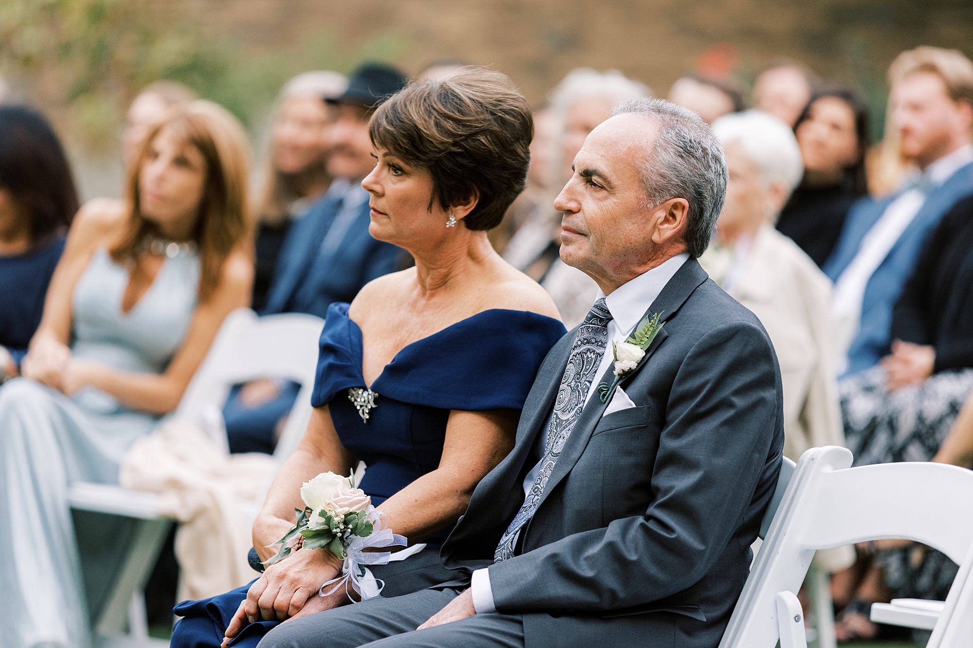 parents hold hands listening to wedding ceremony on lawn