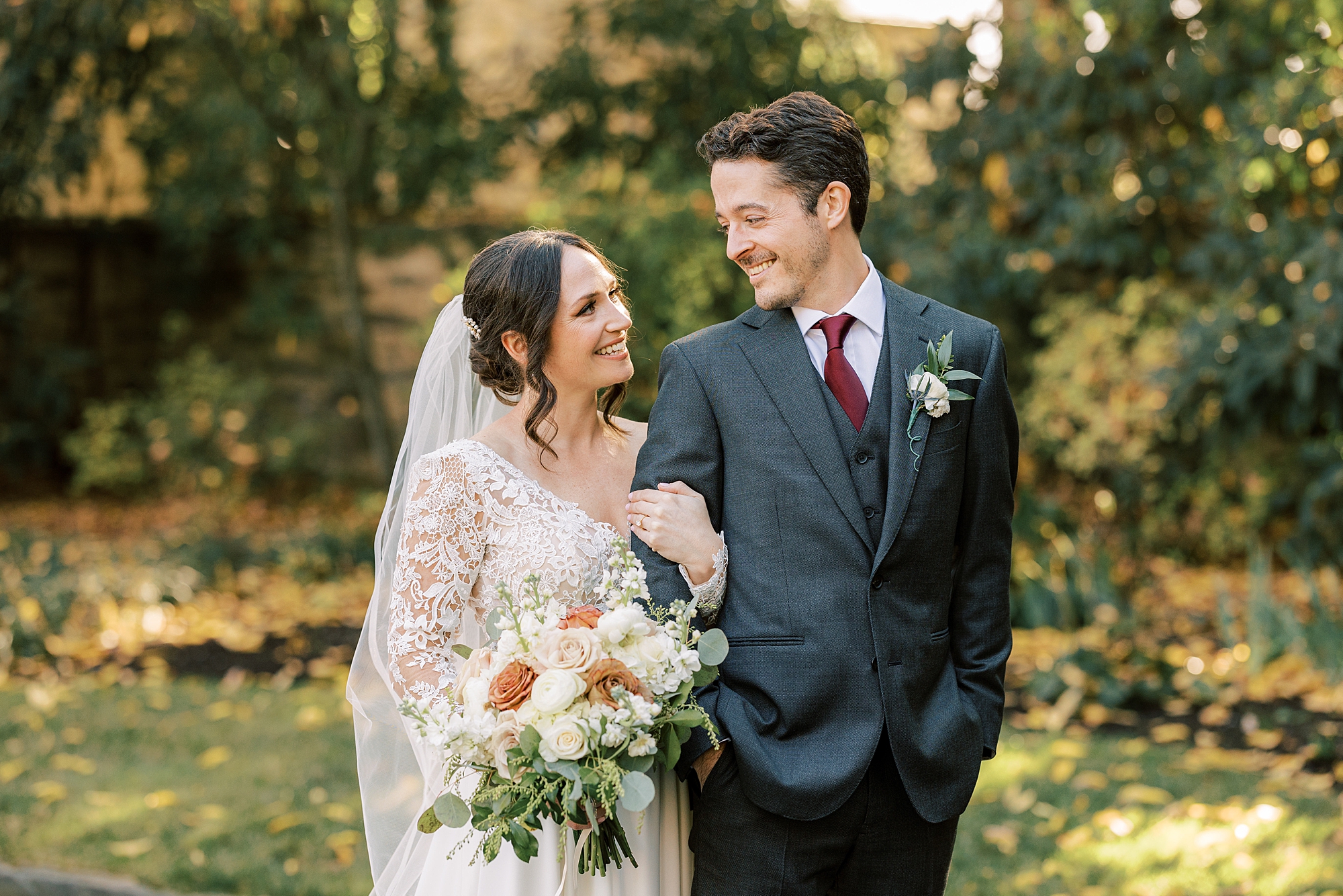 bride holds groom's arm looking up at him during fall wedding portraits