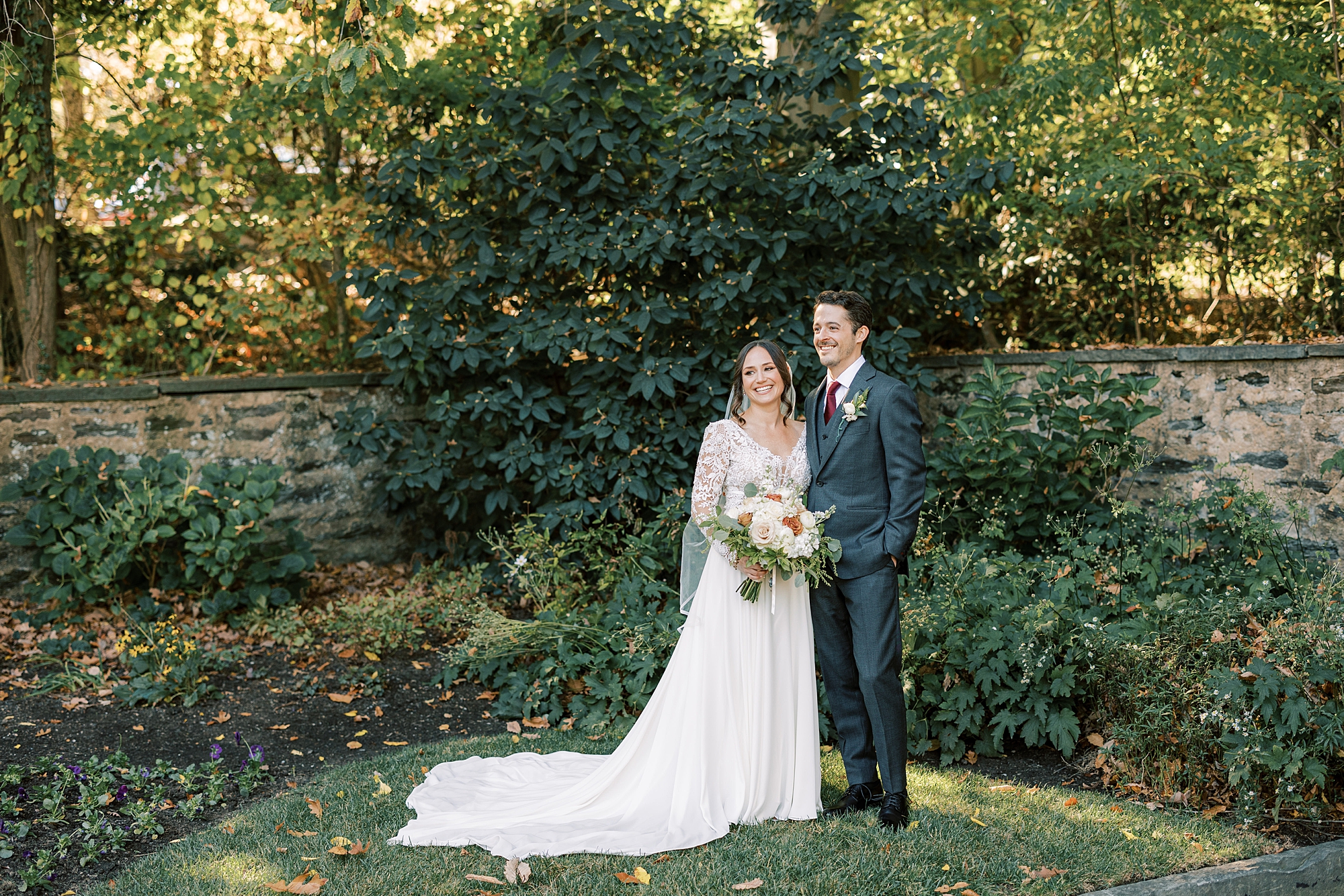 bride and groom stand together in corner of Huntingdon Valley Country Club garden