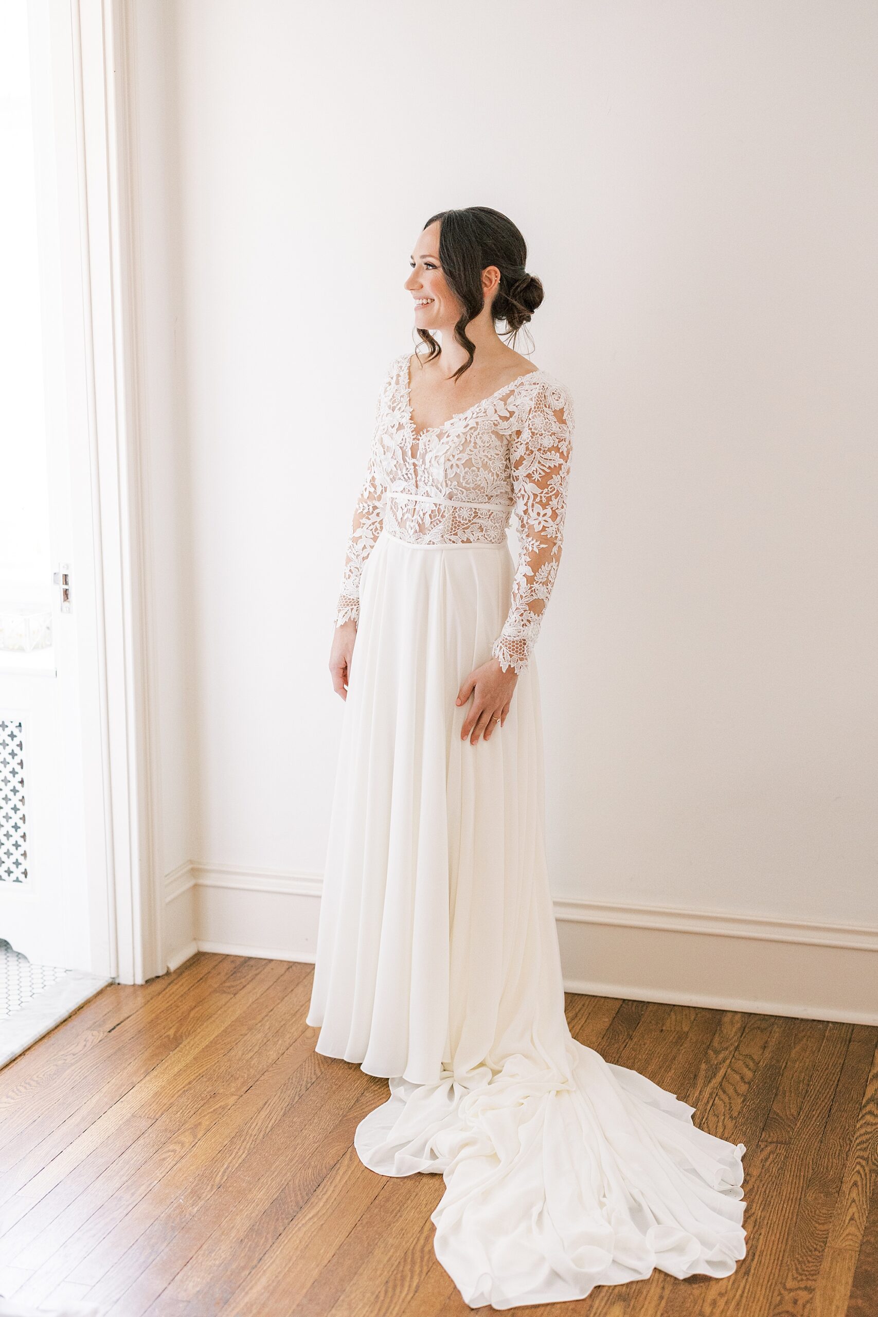 bride poses looking out window in wedding gown with lace sleeves