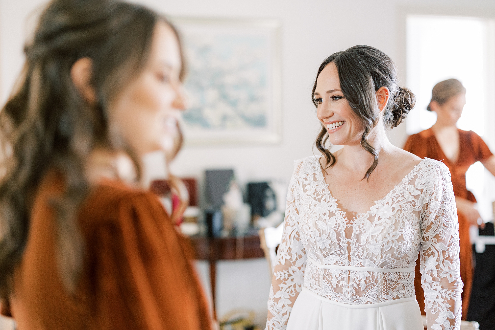 bride smiles talking with bridesmaids in orange velvet gowns before fall wedding
