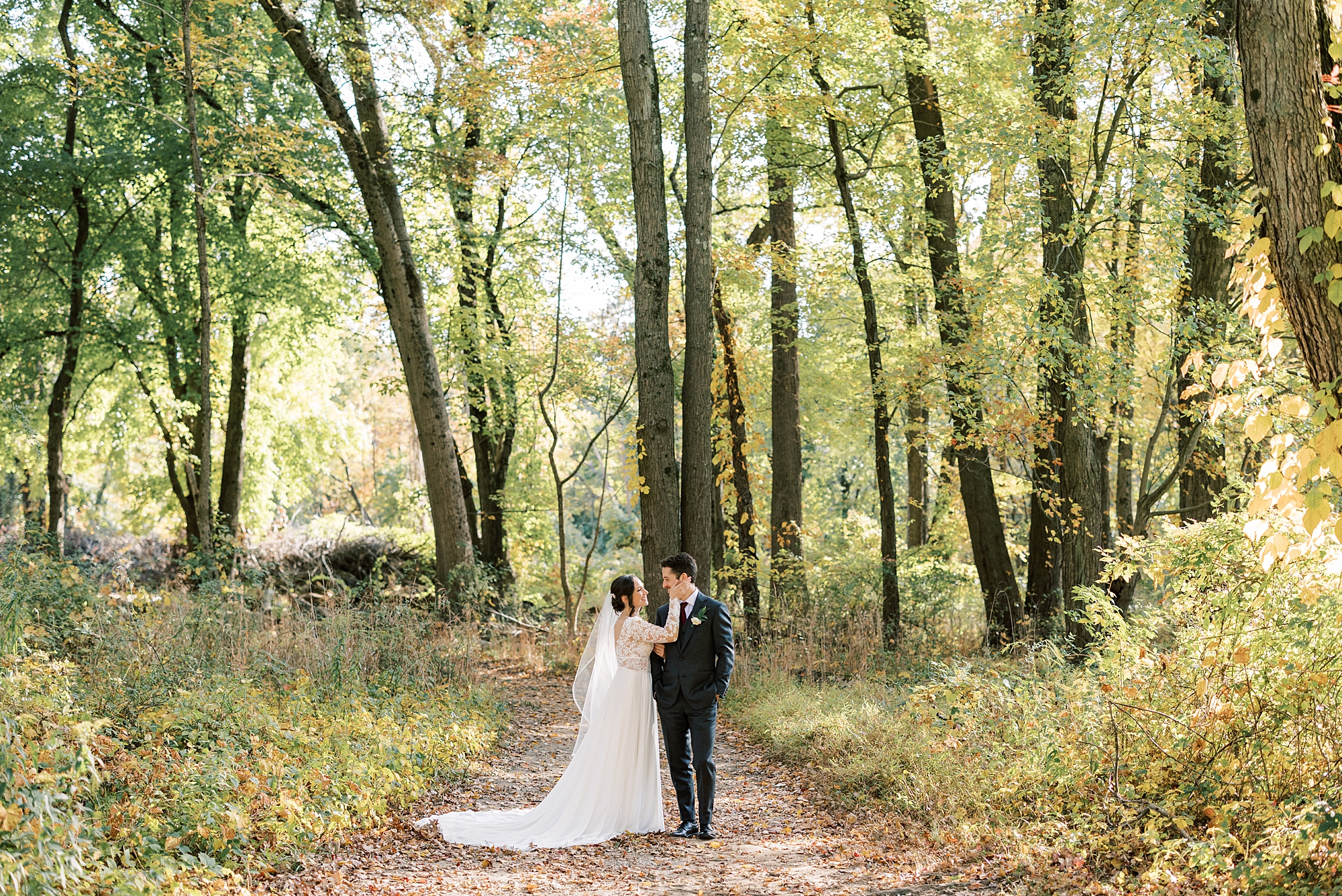 bride and groom hug on path in woods at Huntingdon Valley Country Club