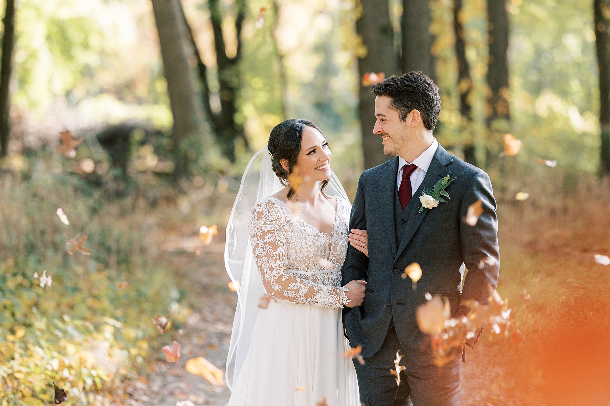 bride smiles up at groom holding his arm during portraits among trees at Huntingdon Valley Country Club
