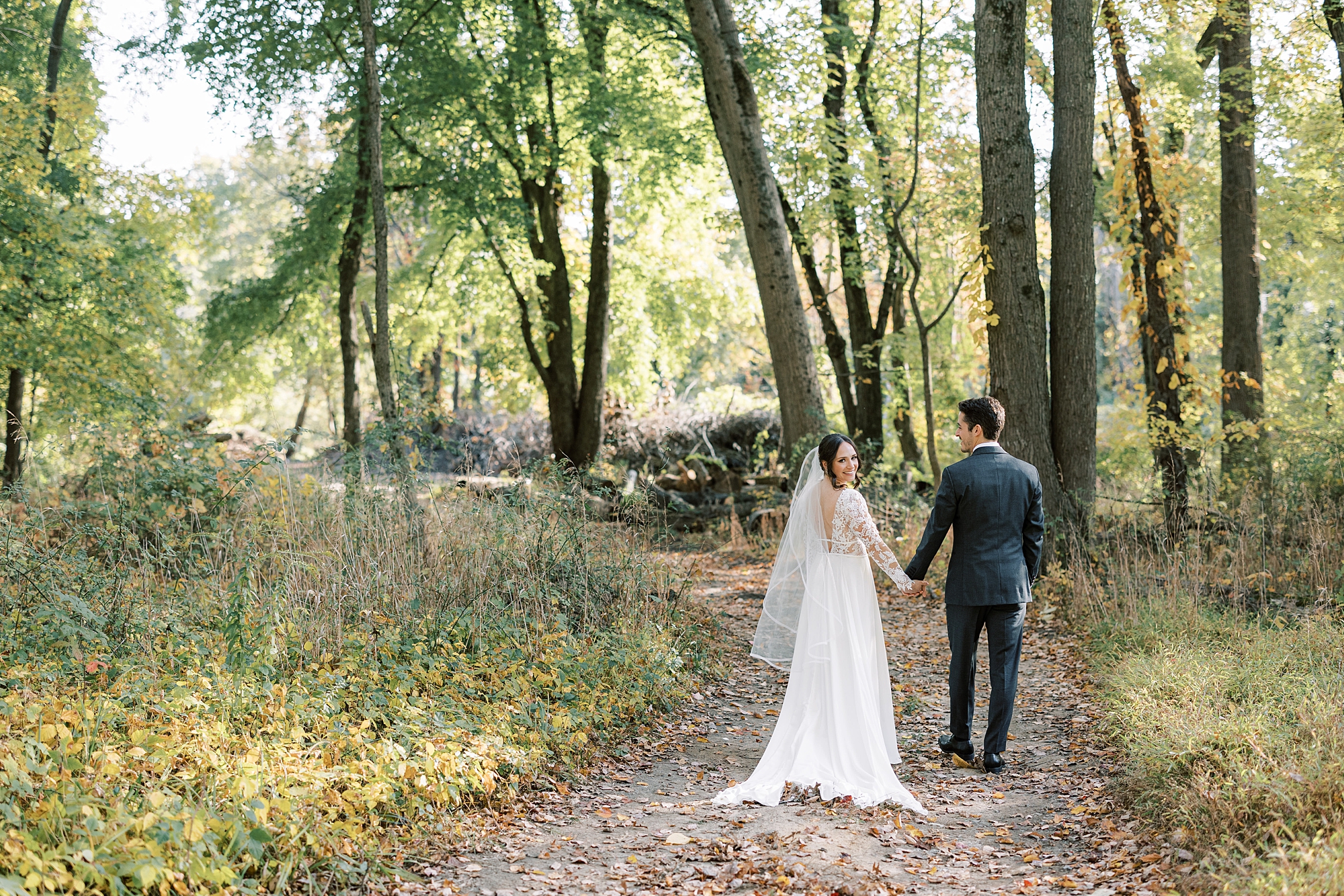 bride and groom hold hands walking through path in woods at Huntingdon Valley Country Club