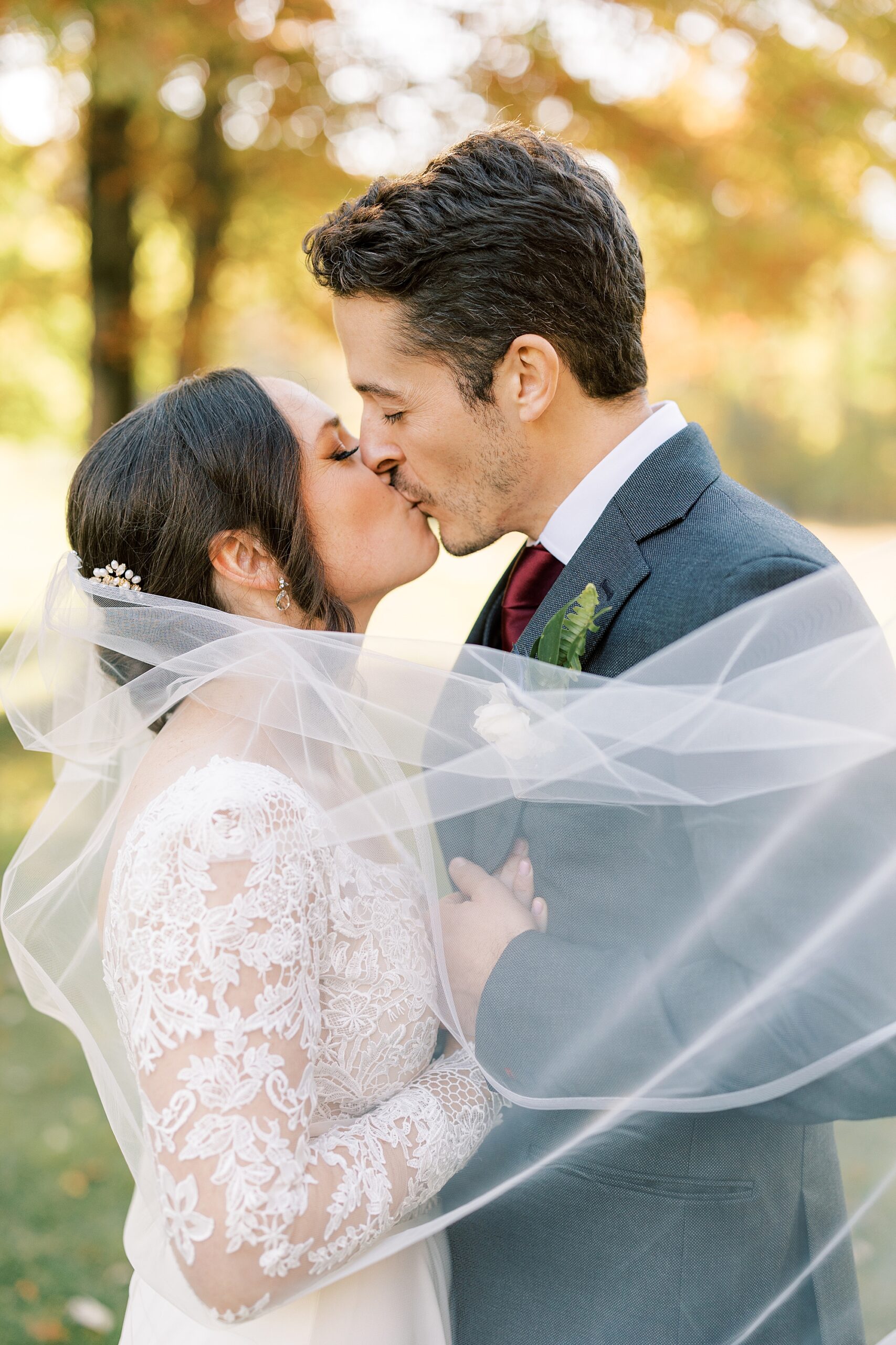 bride and groom kiss with veil wrapped around them