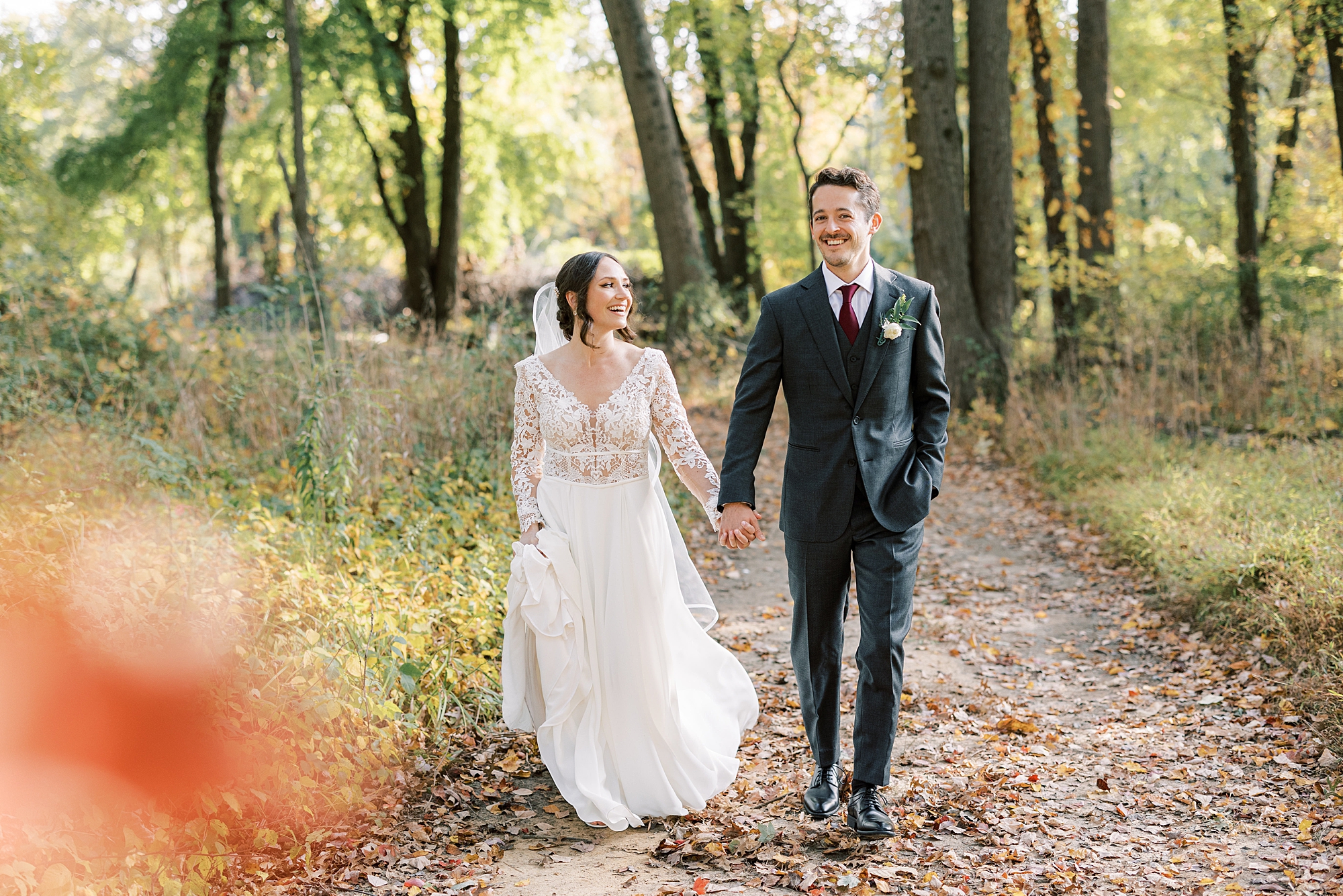 bride and groom hold hands walking down path in woods