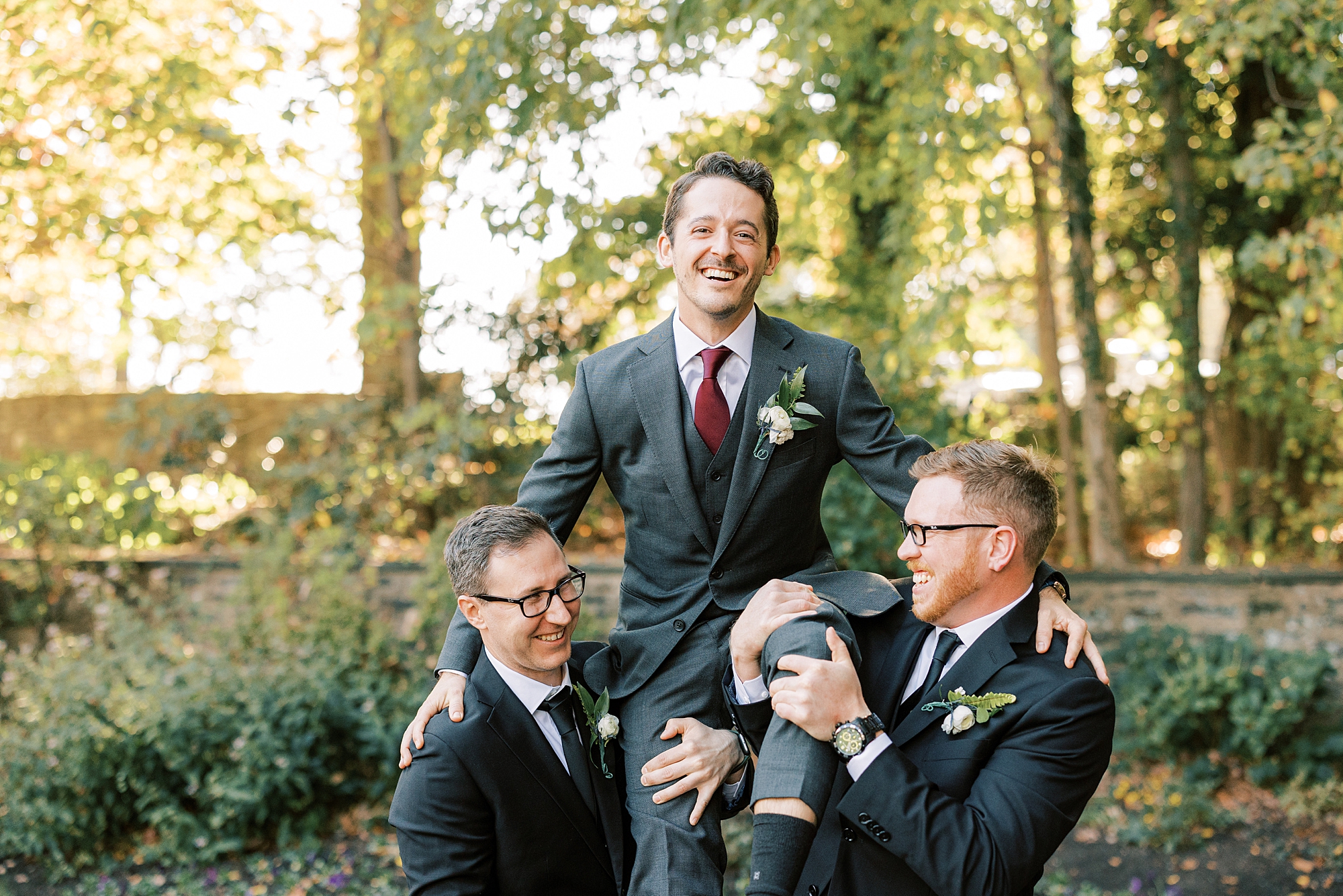 groomsmen lift groom up on their shoulders on lawn at Huntingdon Valley Country Club