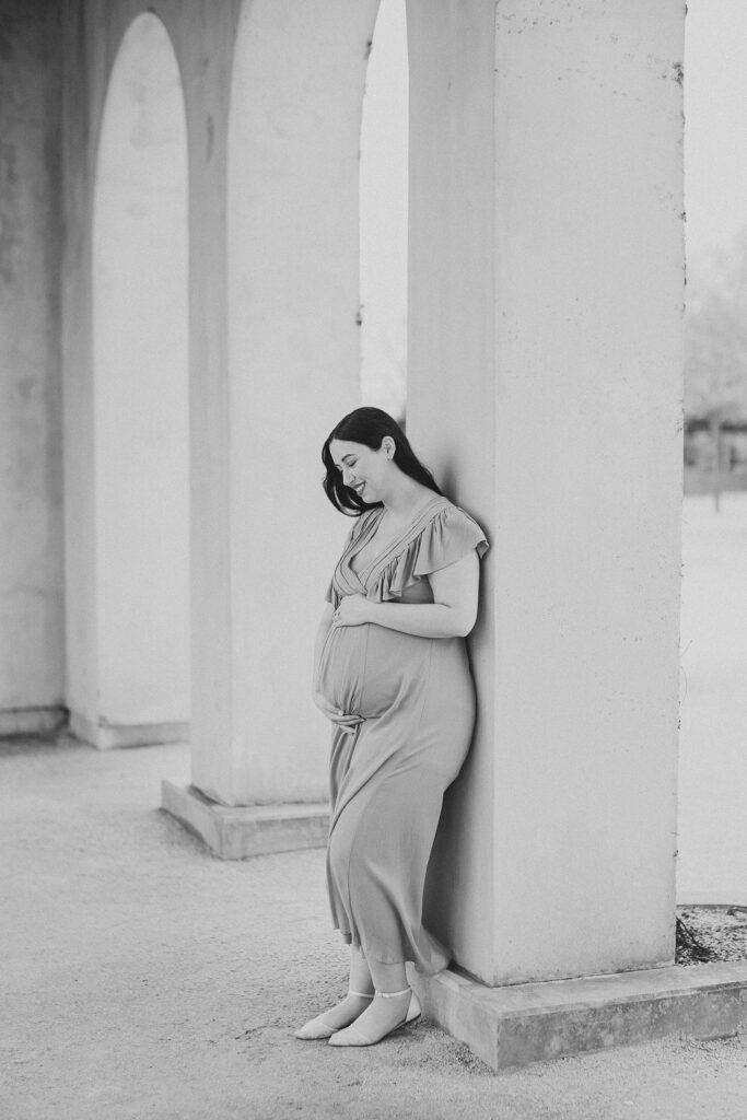 mother leans against pillar at Longwood Gardens holding baby bump