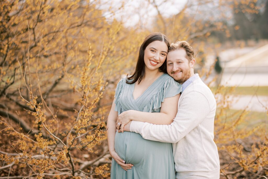 man hugs wife around baby belly during Longwood Gardens maternity portraits