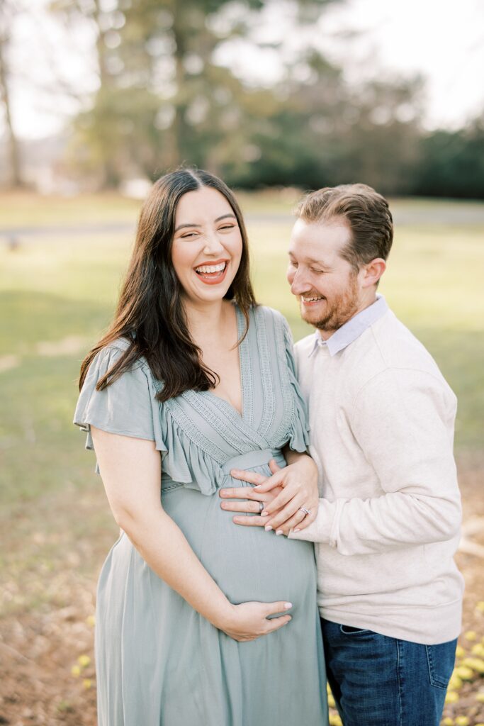 expecting parents laugh holding hands on mom's baby bump