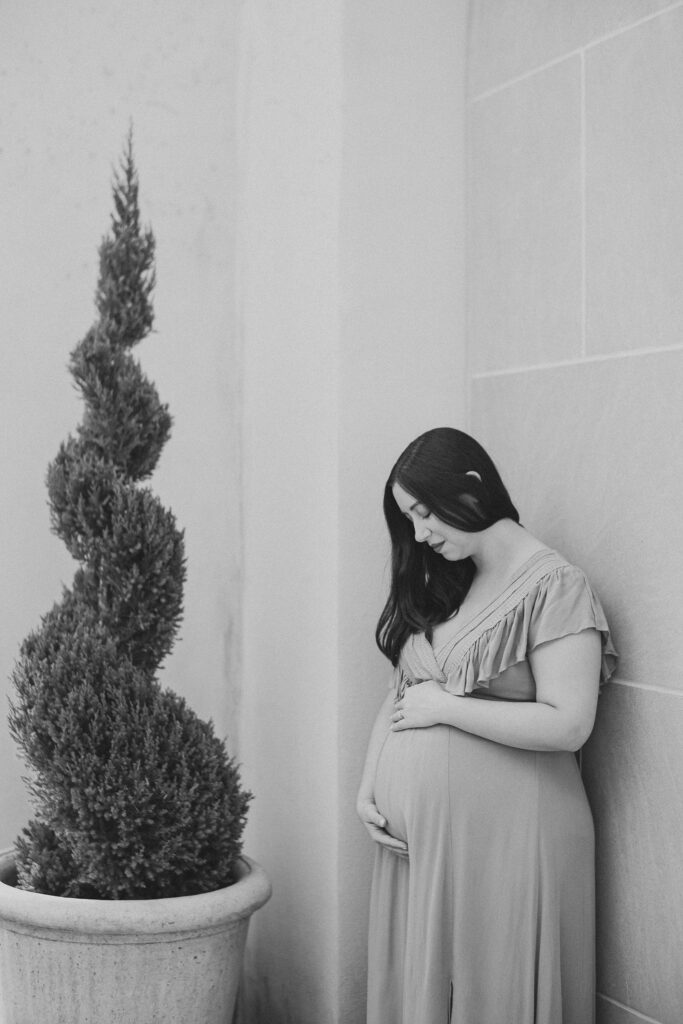 expecting mother looks down at baby bump against wall at Longwood Gardens