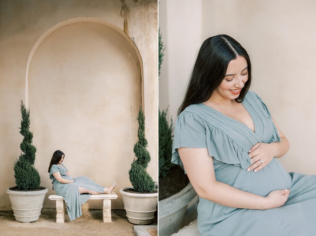 woman in sage green maternity gown holds baby bump sitting by wall at Longwood Gardens
