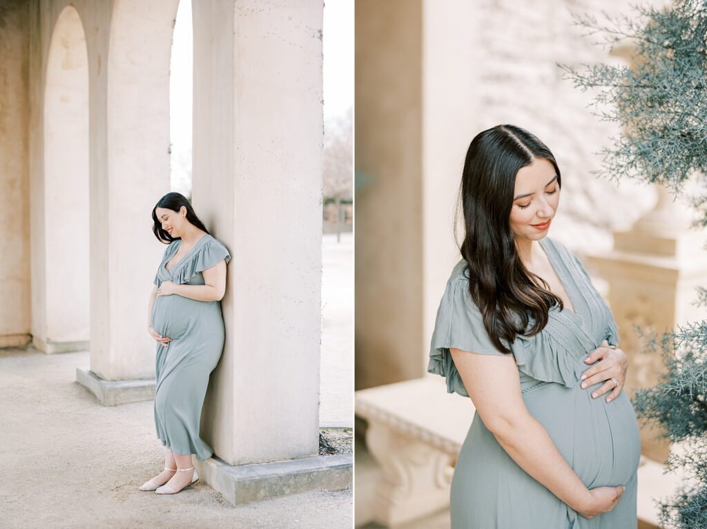 woman leans against column at Longwood Gardens holding baby bump in sage green gown