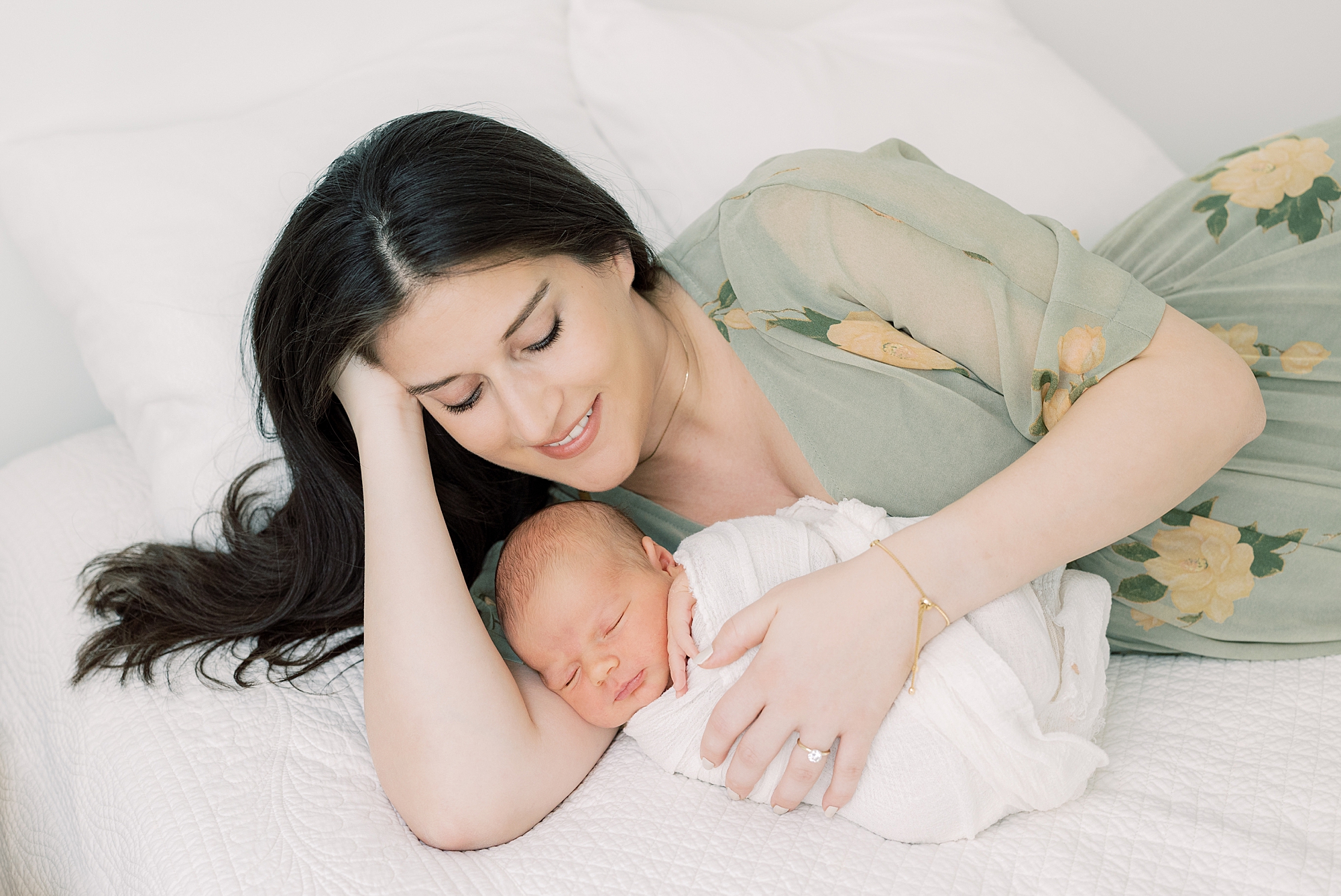 mother in green dress holds baby to her laying on bed