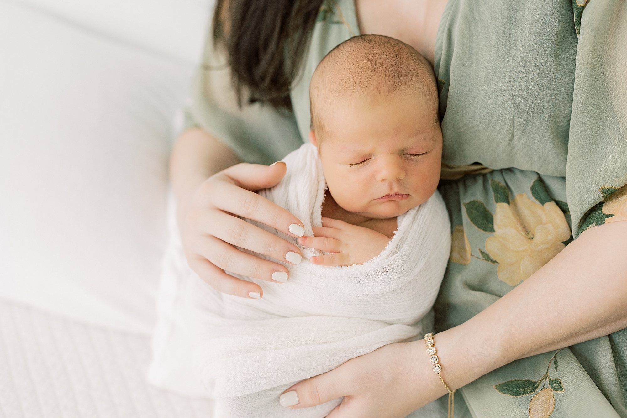 mom in green dress holds son in white wrap to her during PA newborn portraits at home