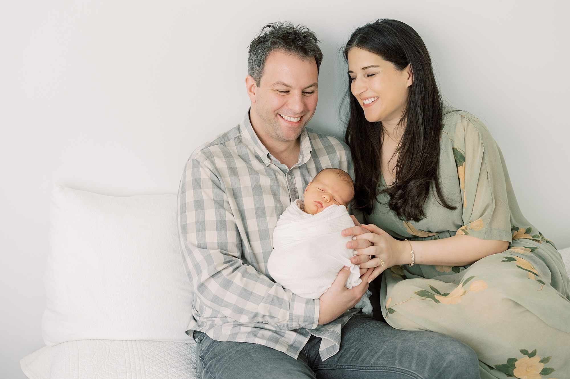 parents laugh holding new son during photos on bed