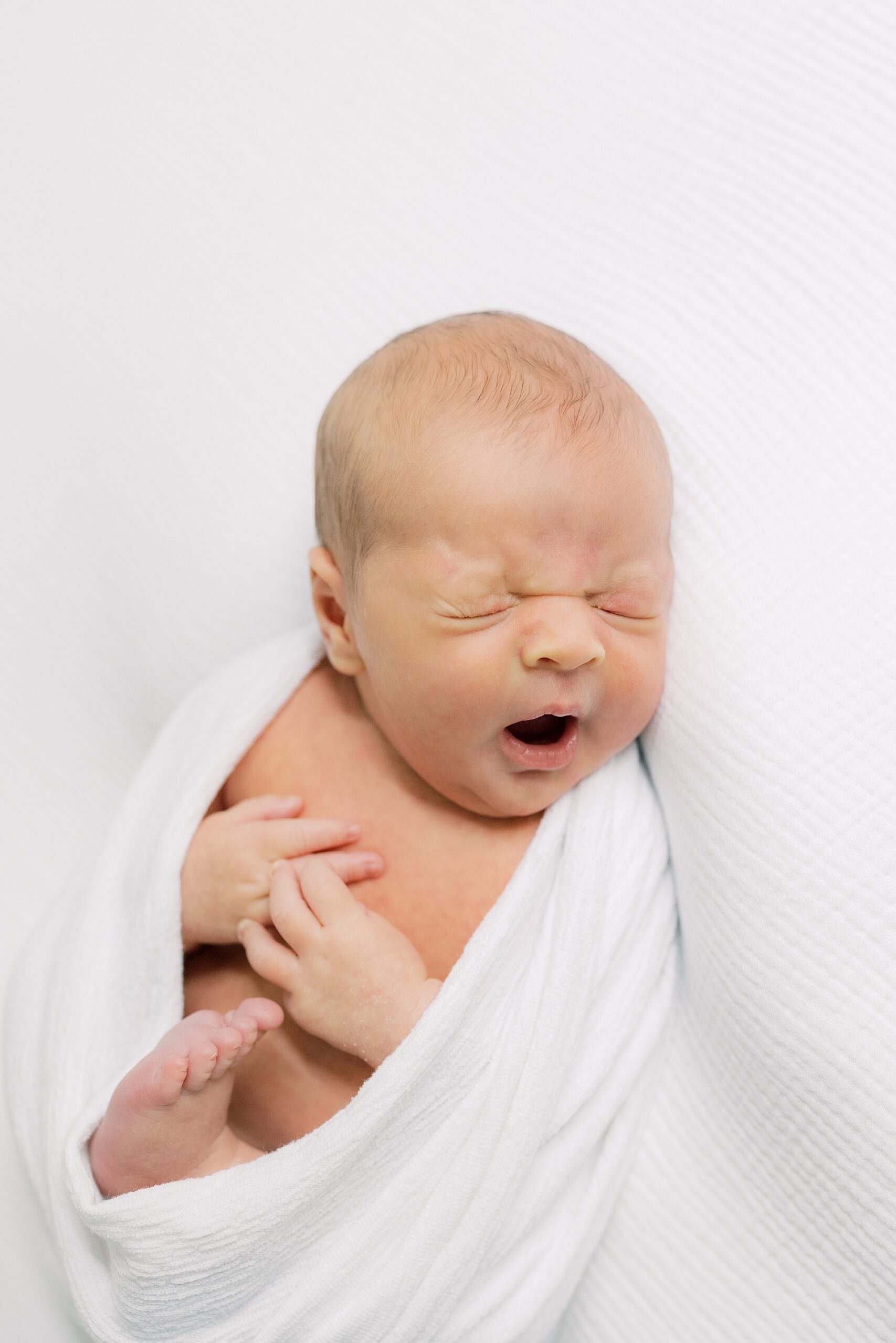 baby boy yawns during newborn portraits in white wrap 