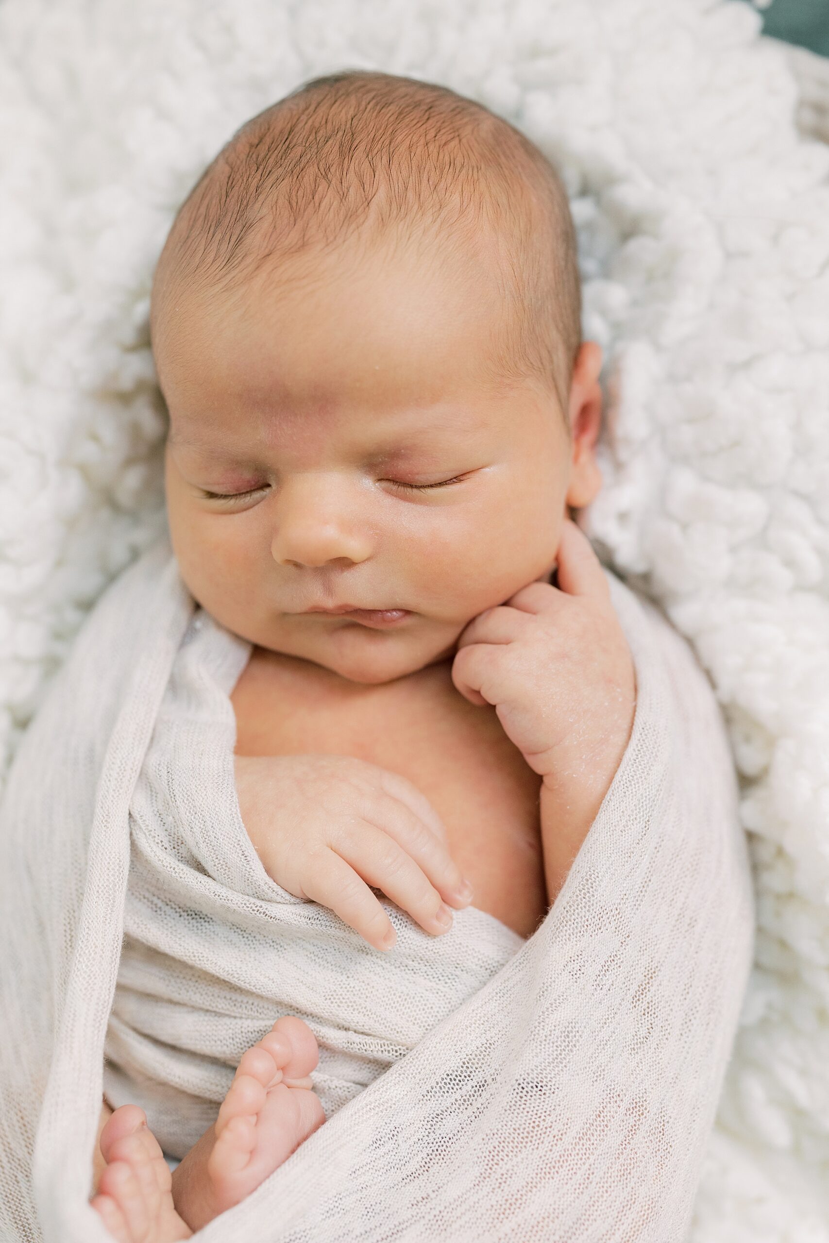 baby sleeps with hand under chin in white wrap during PA newborn portraits at home