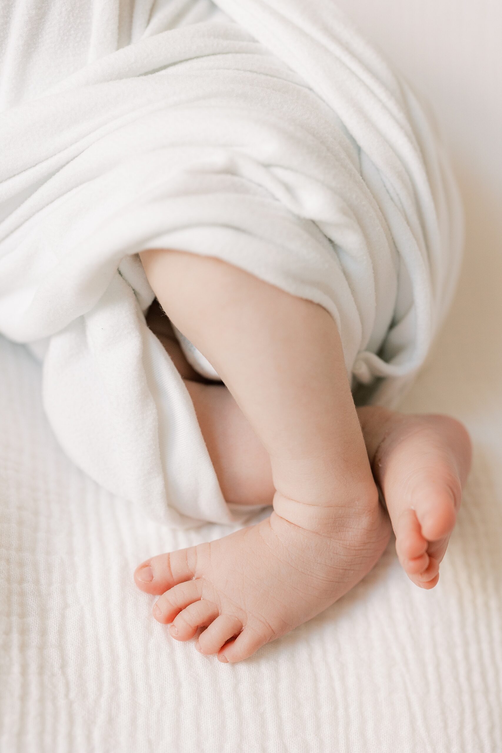 baby girl's feet stick out of white blankets during studio newborn session in Philadelphia PA
