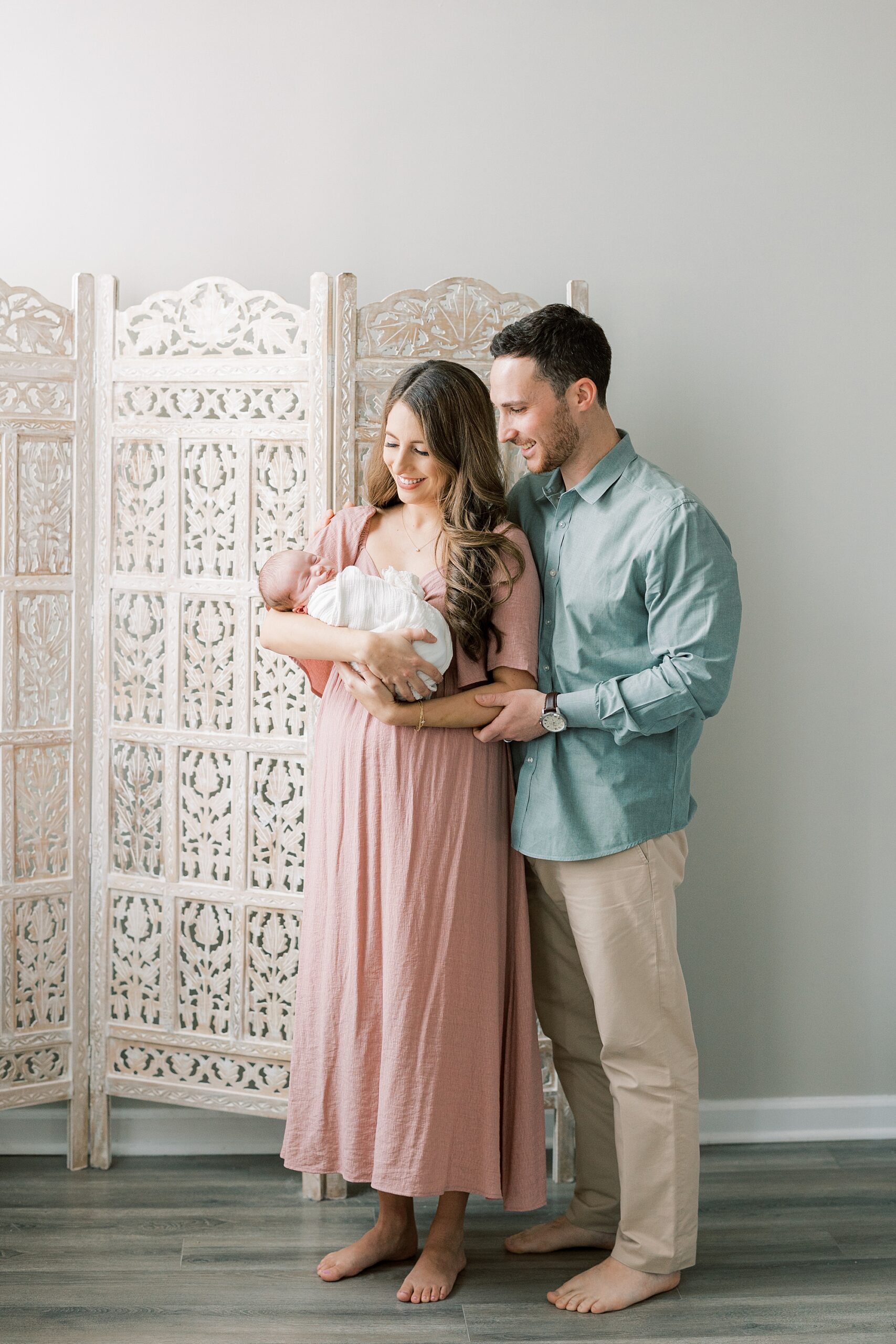 new parents hug baby girl by room divider during studio newborn session in Philadelphia PA