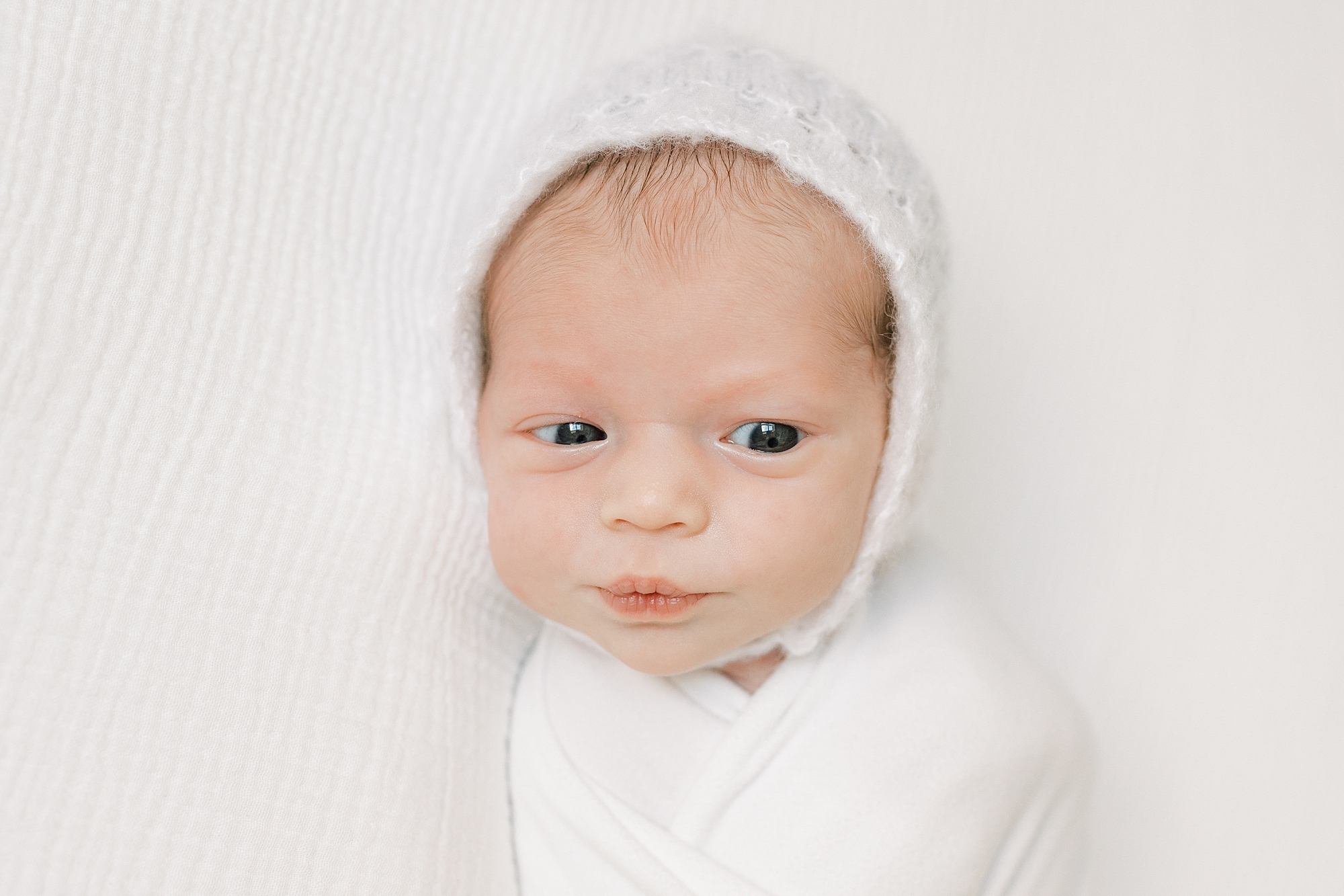 baby girl lays on white blanket in white knit cap