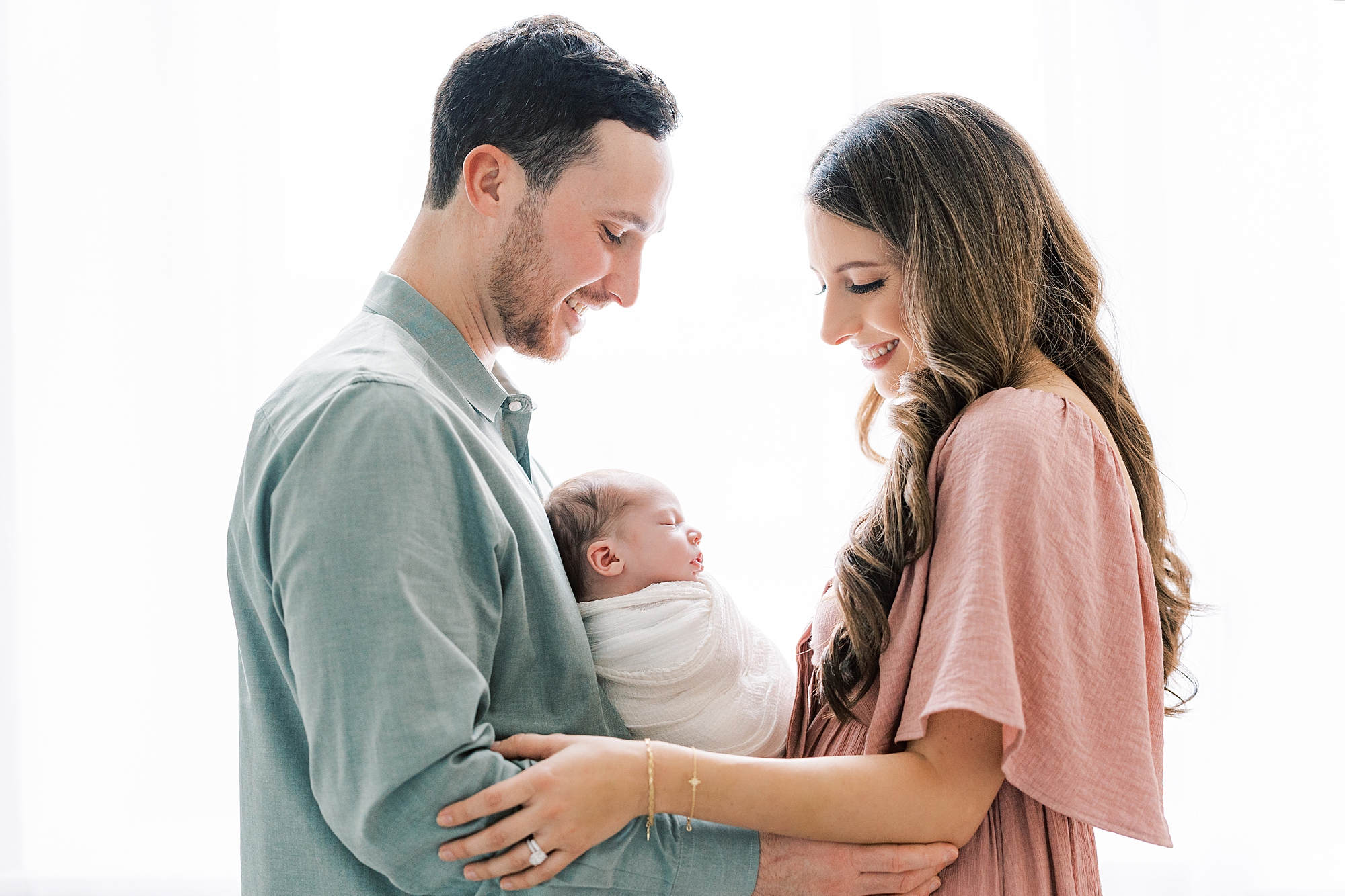 parents hold newborn daughter between them against white wall in studio 