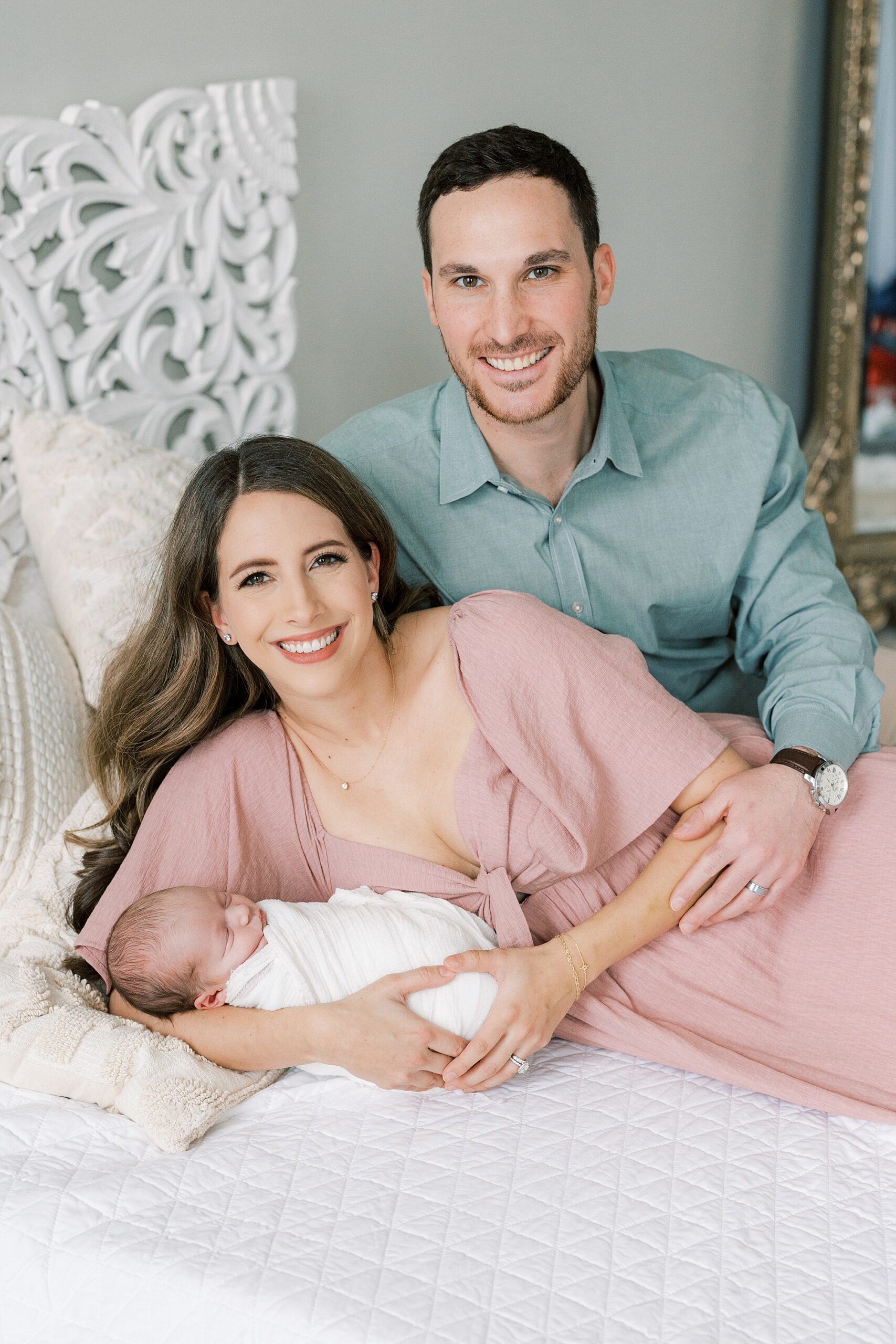 couple lays on bed during studio newborn session in Philadelphia PA with baby girl in front of them 