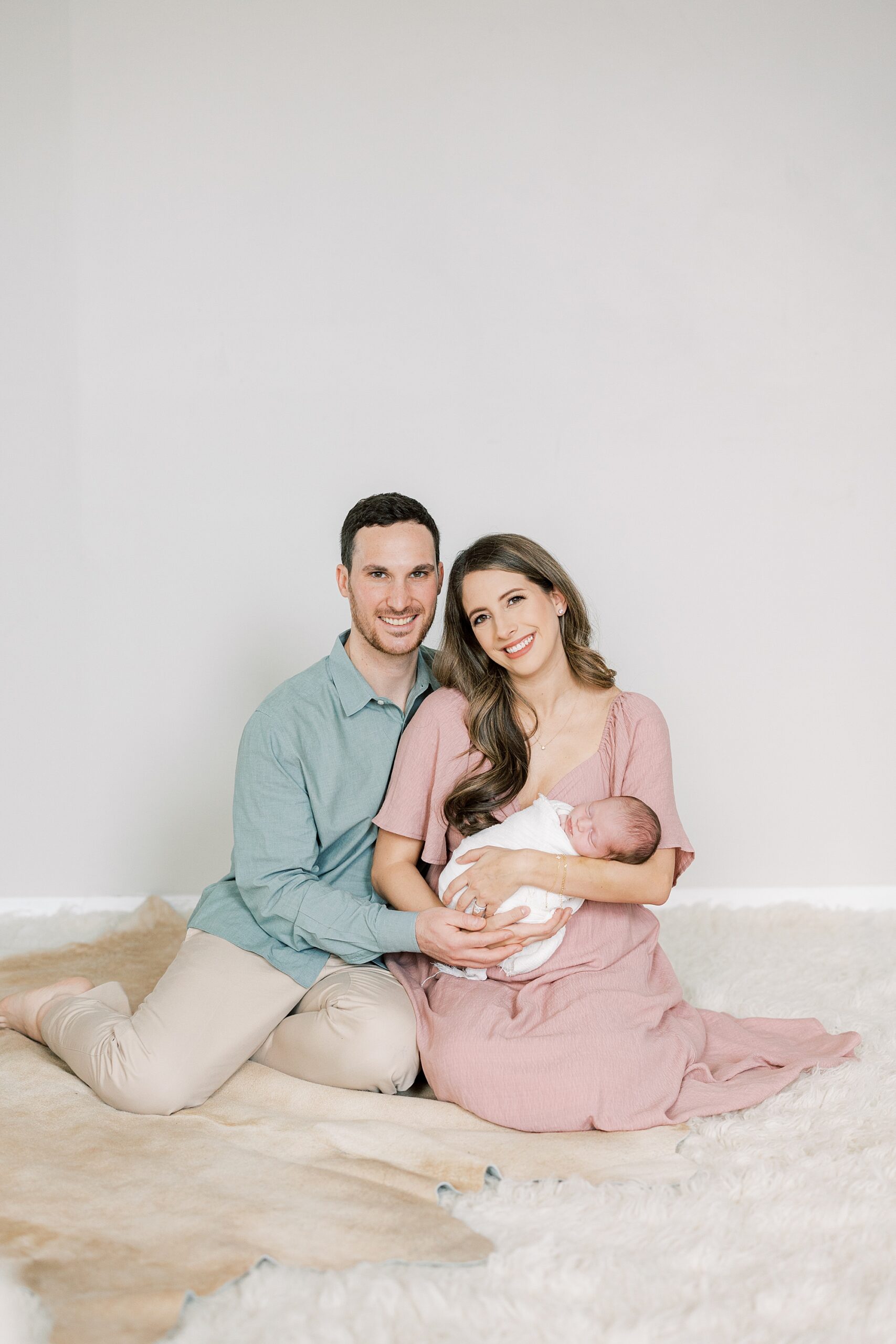 parents sit on floor holding baby girl during studio newborn session in Philadelphia PA