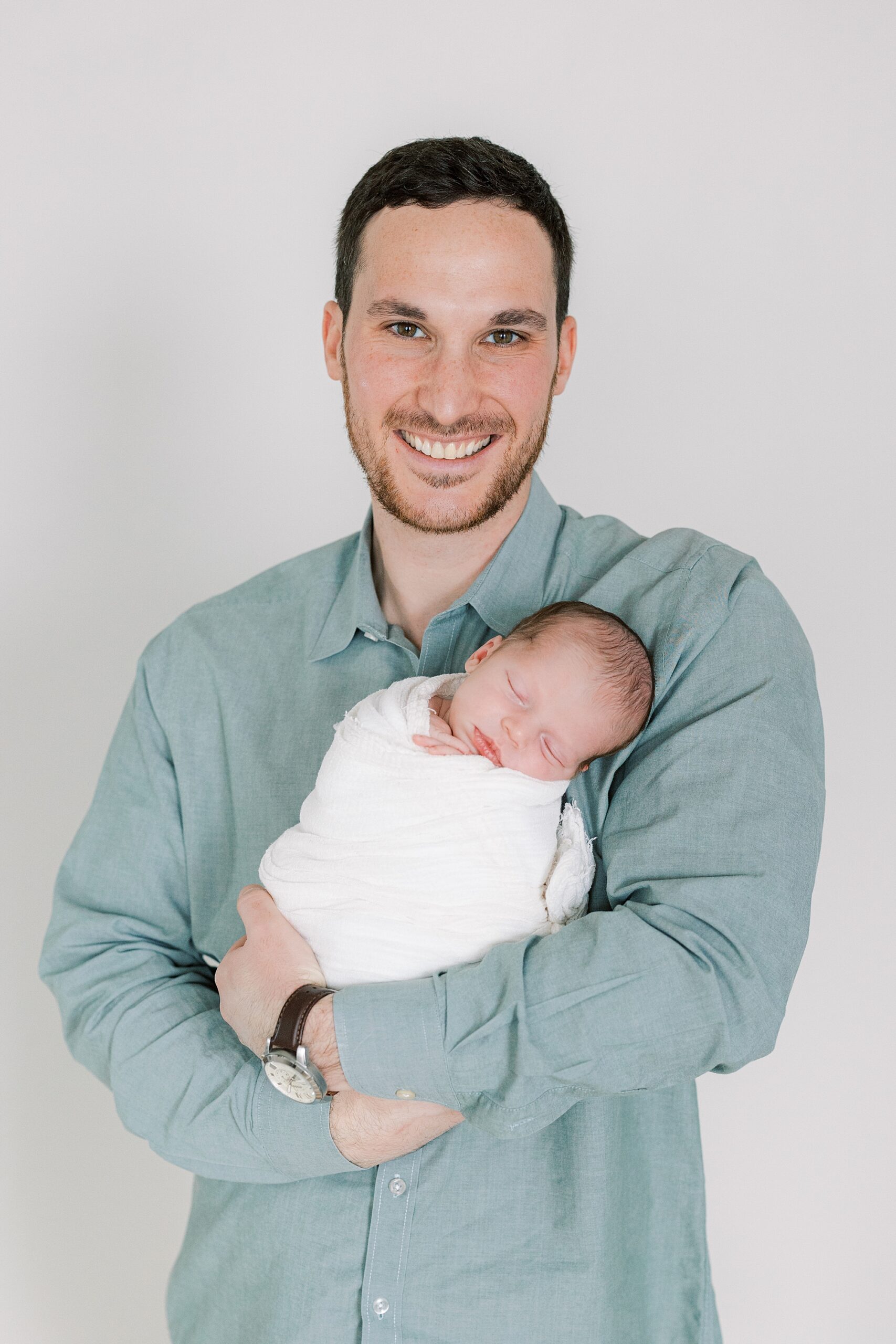 man in green shirt holds newborn daughter wrapped in white blanket 