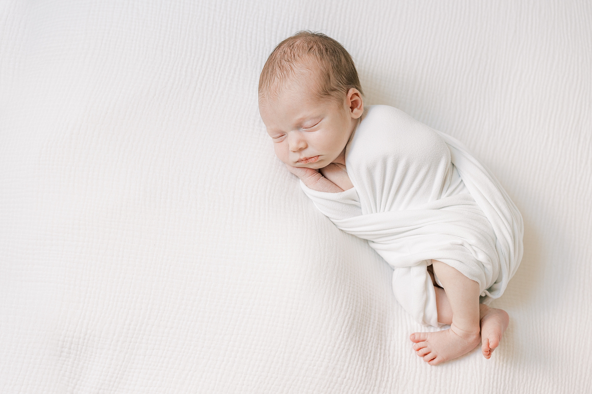 baby lays in white wrap during studio newborn session 