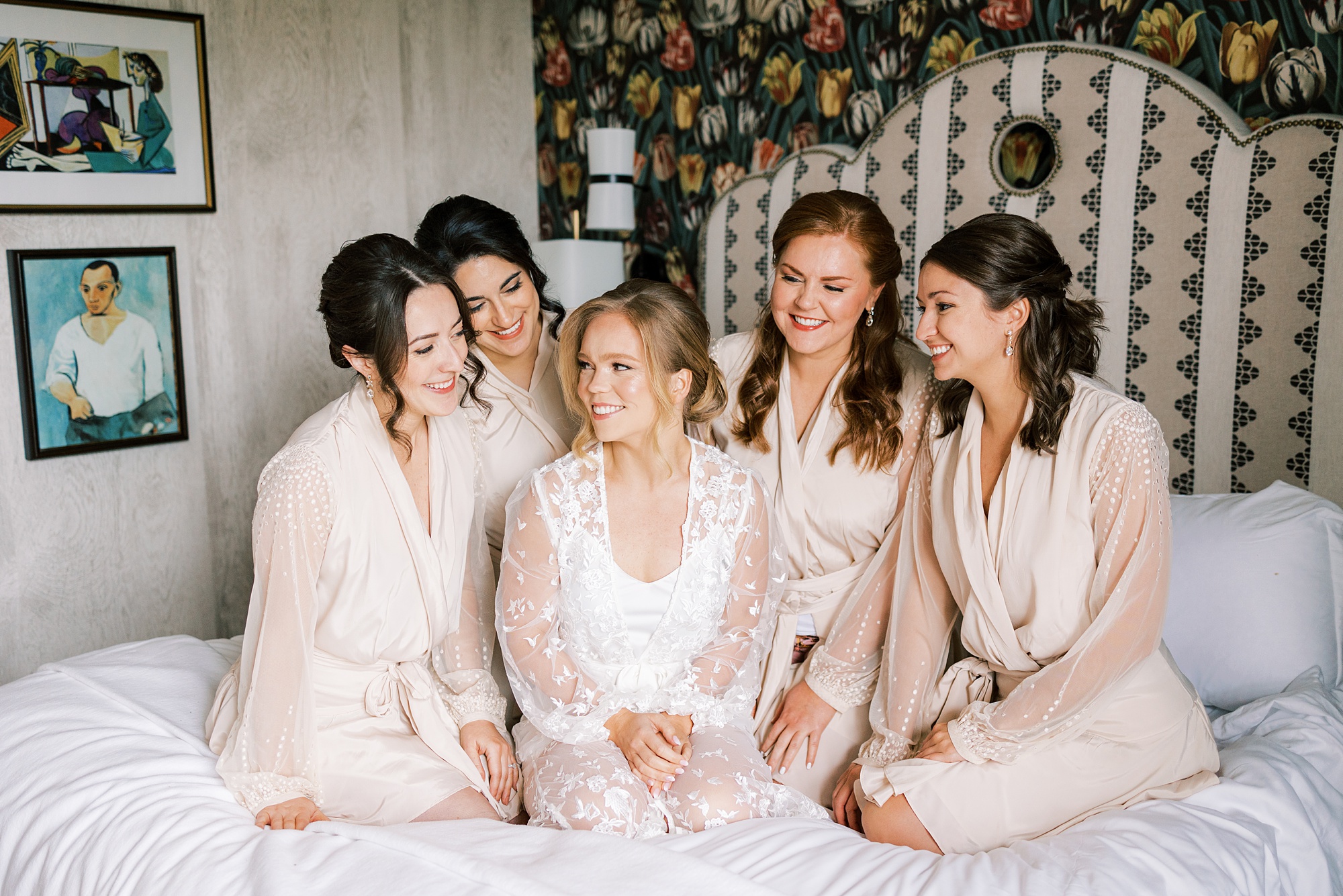 bride sits with bridesmaids in matching robes on bed at The River House at Odette's
