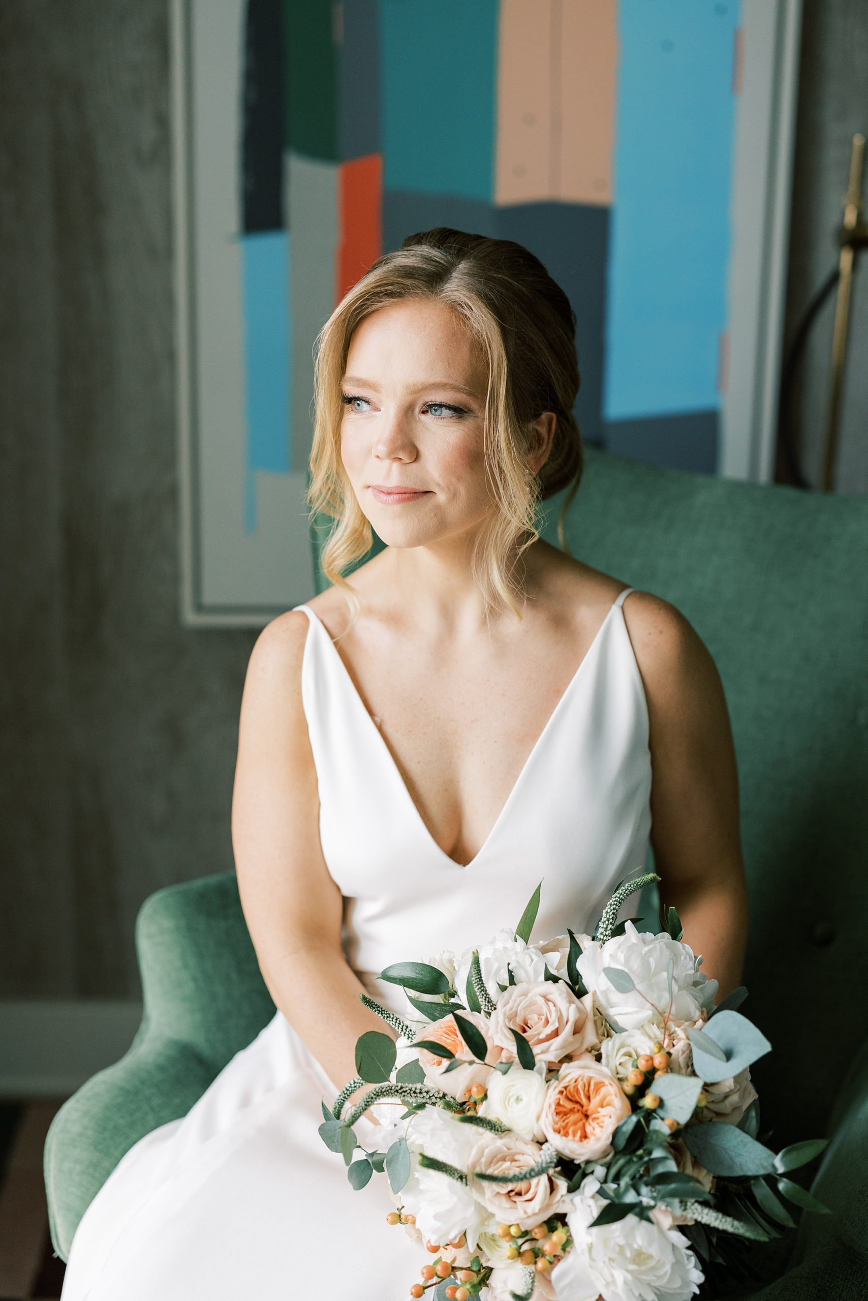 bride sits on green chair holding bouquet with peach peonies 
