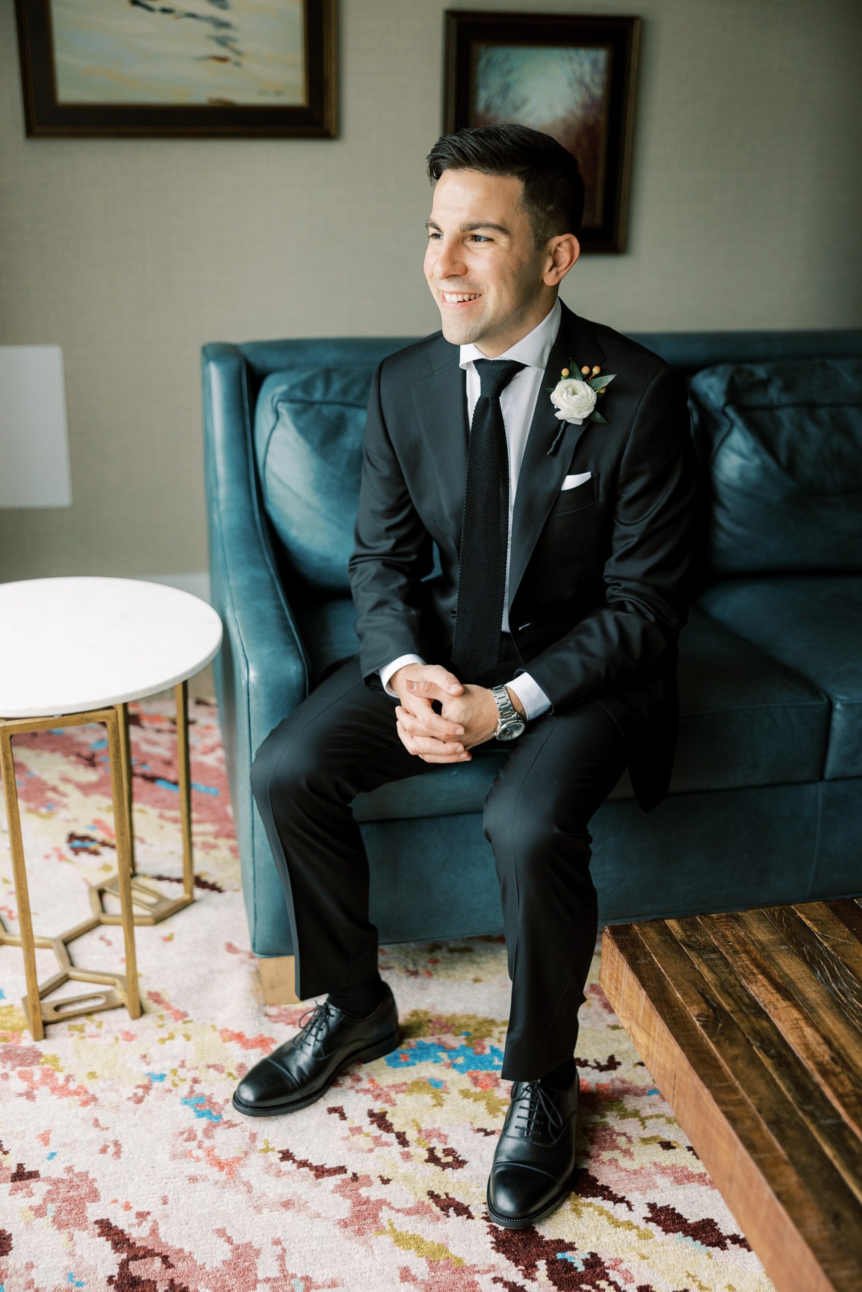 groom sits on teal couch in room at The River House at Odette's