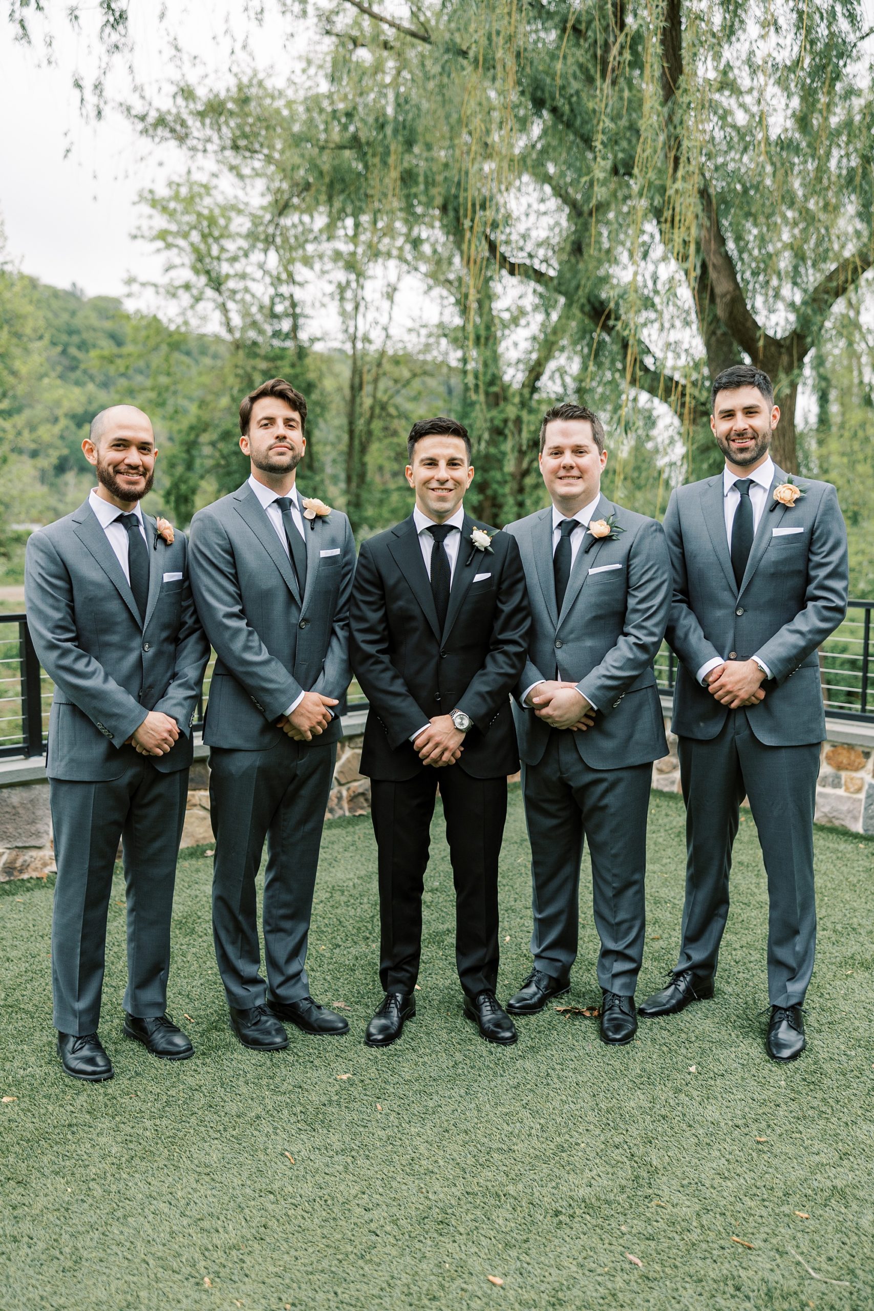 groom poses with groomsmen in grey suits on lawn at The River House at Odette's