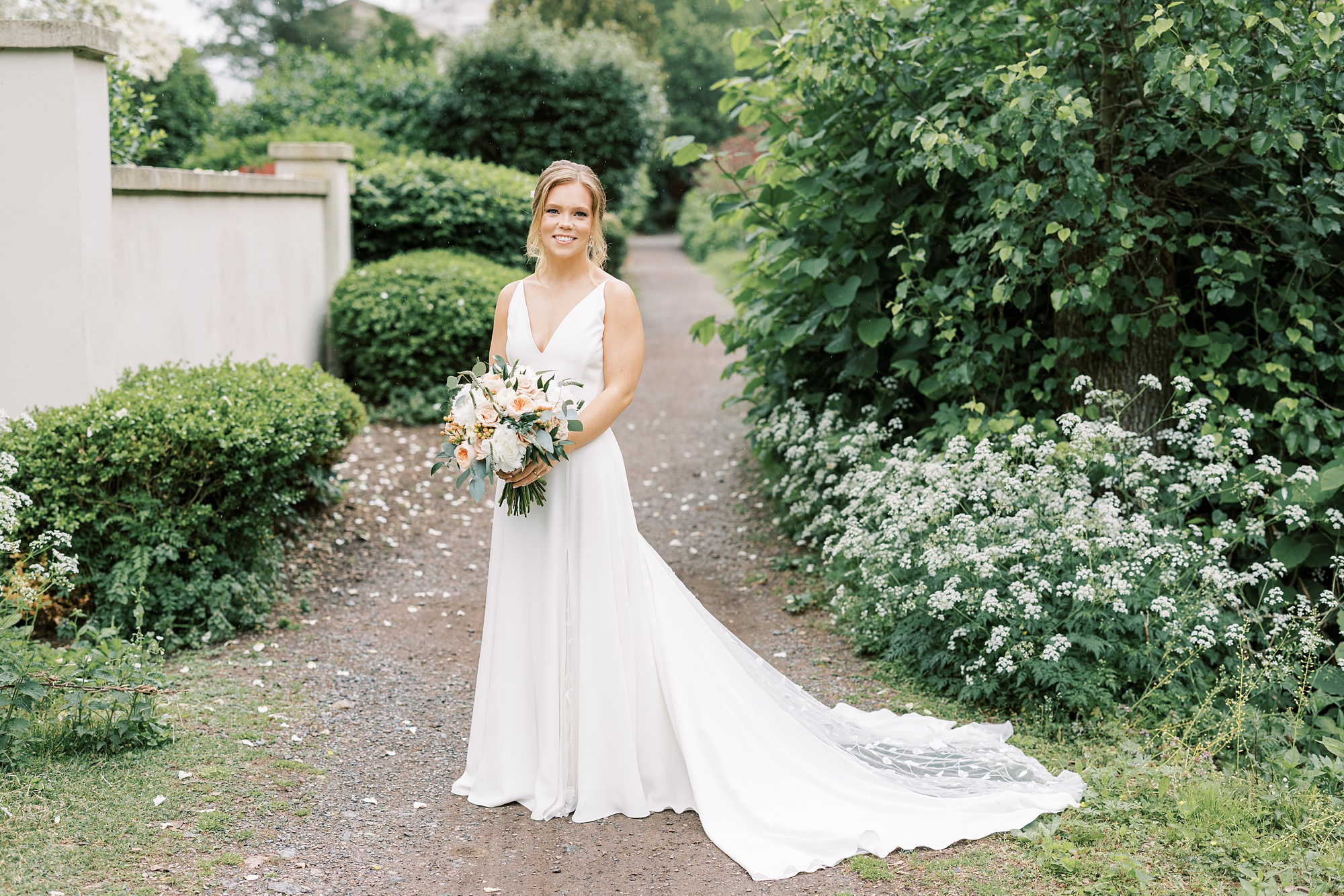 bride stands in front of bushes by The River House at Odette's