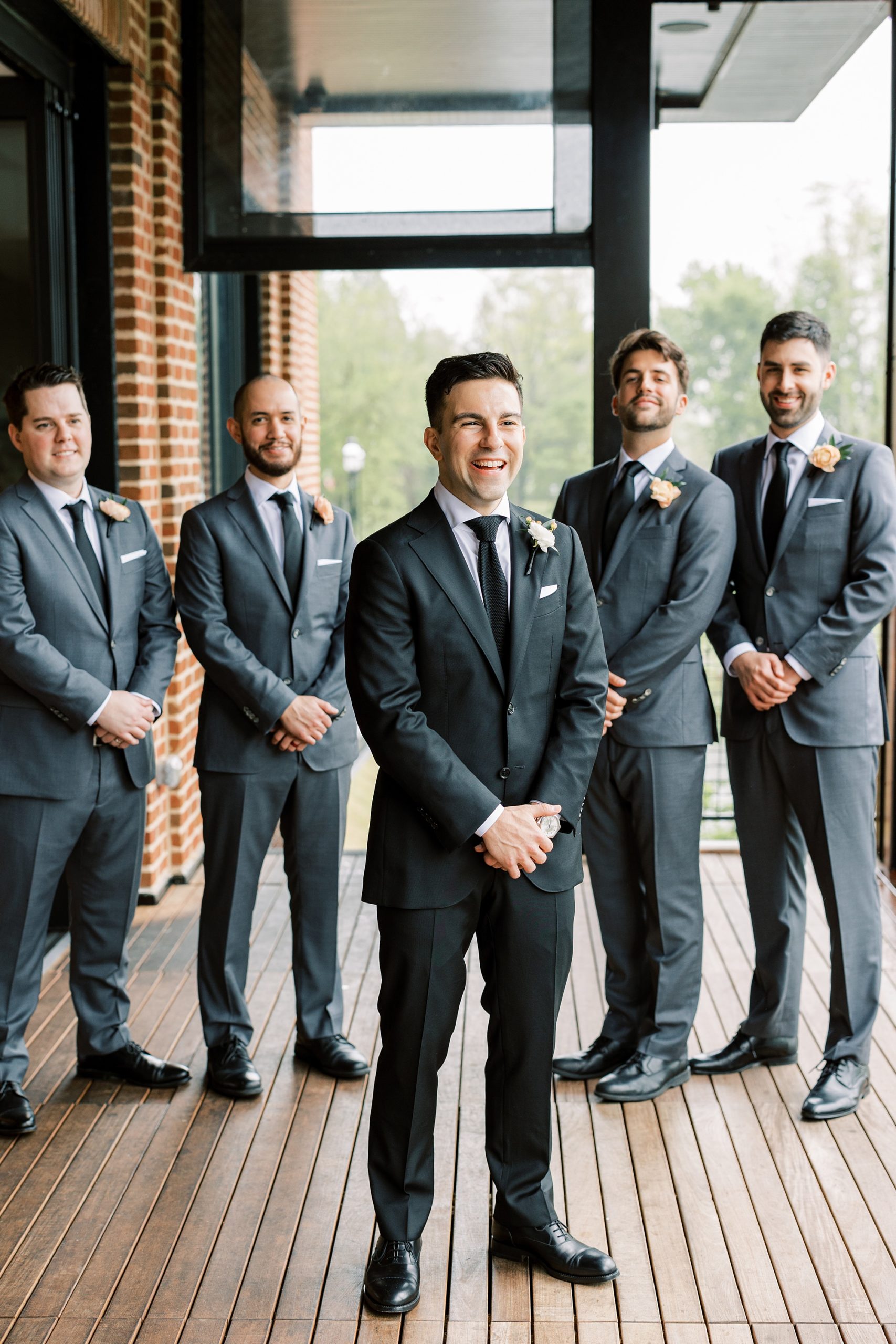 groom stands with groomsmen in grey suits on patio at The River House at Odette's