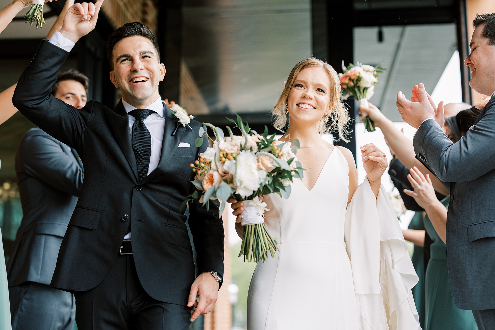 newlyweds laugh walking between bridal party clapping for them 